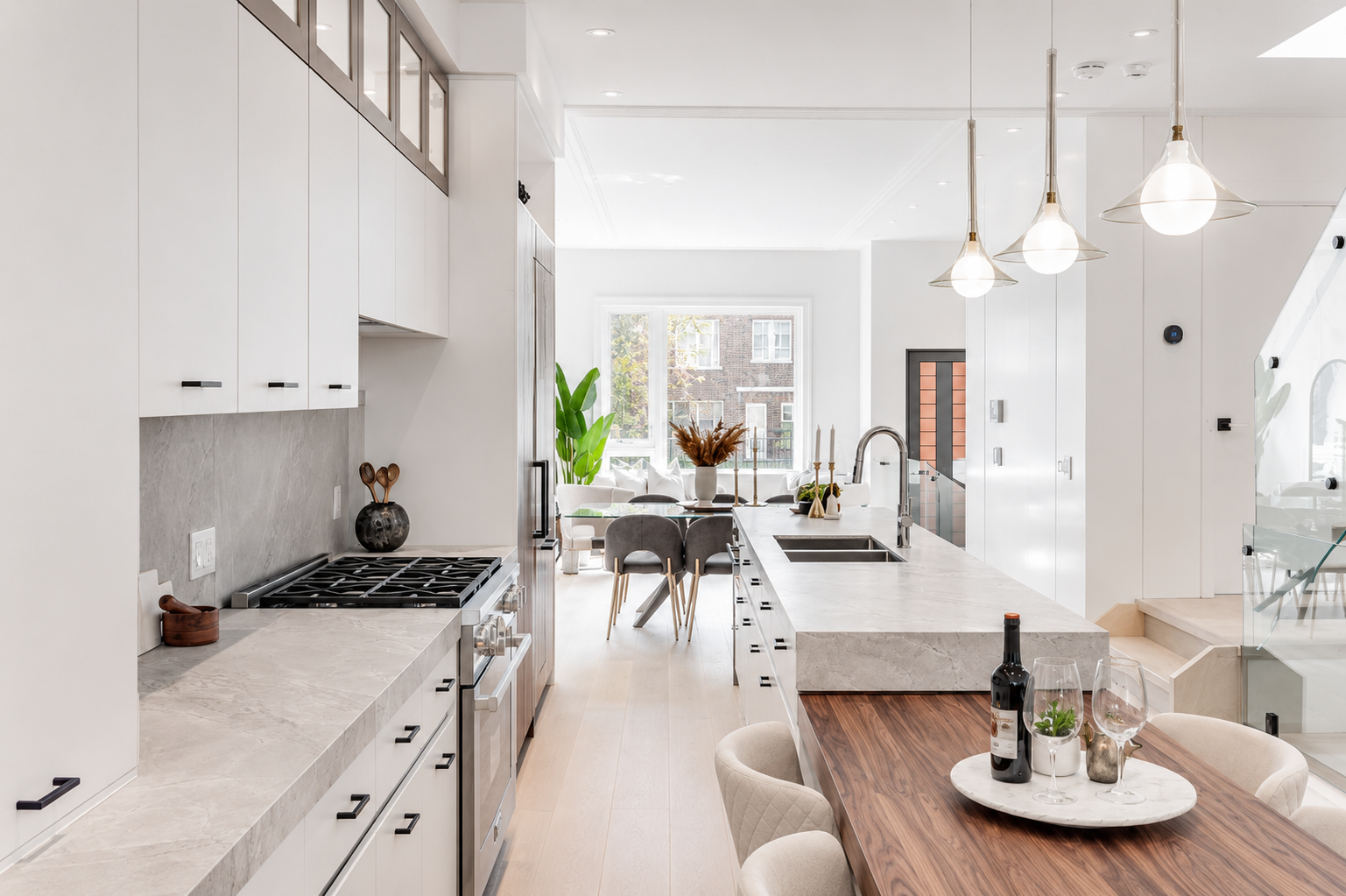 Open kitchen with white cabinetry, marble island, wood dining table, and pendant lights