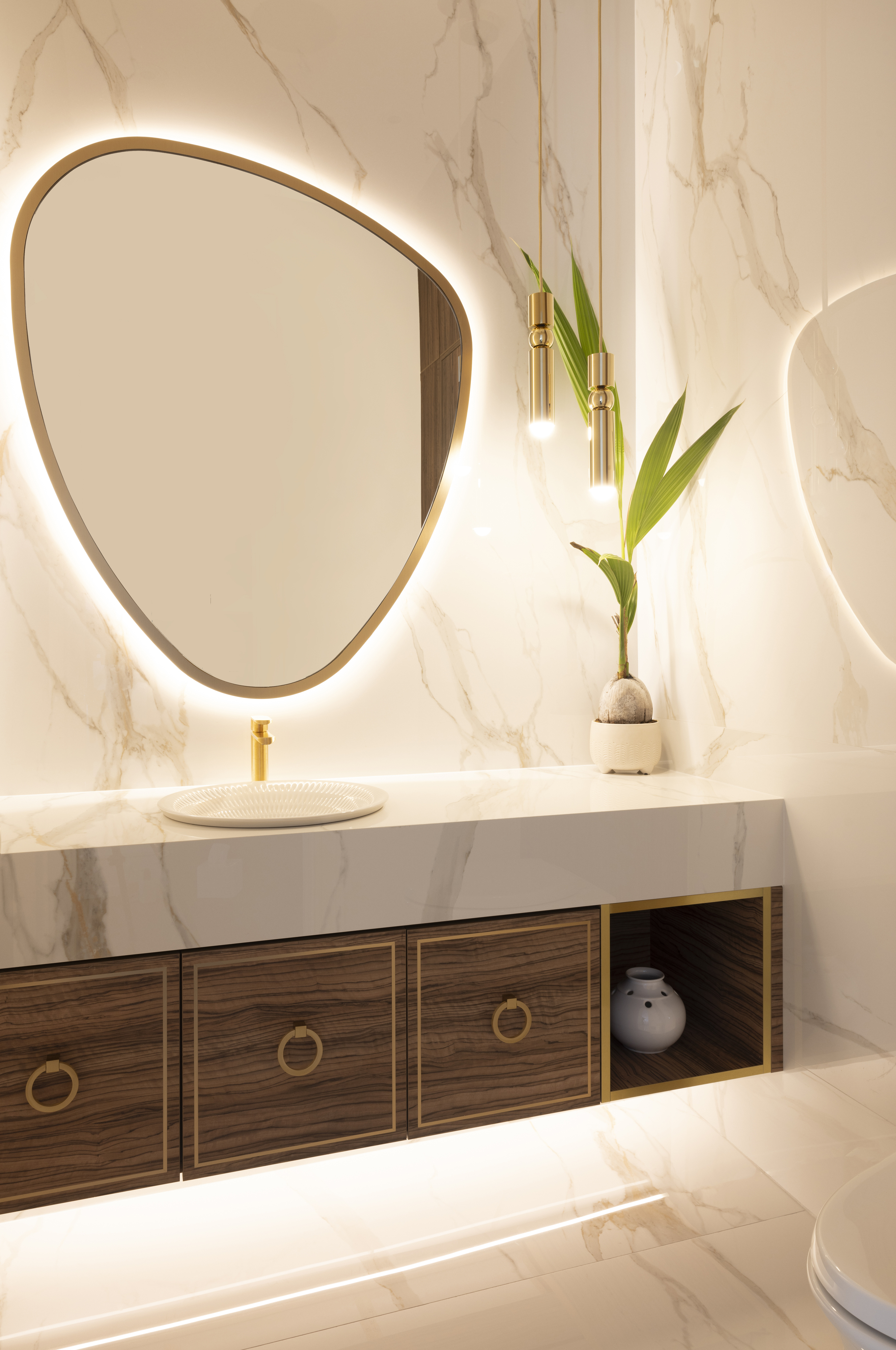 Room with marble vanity, backlit oval mirror, wood cabinetry, and gold fixtures