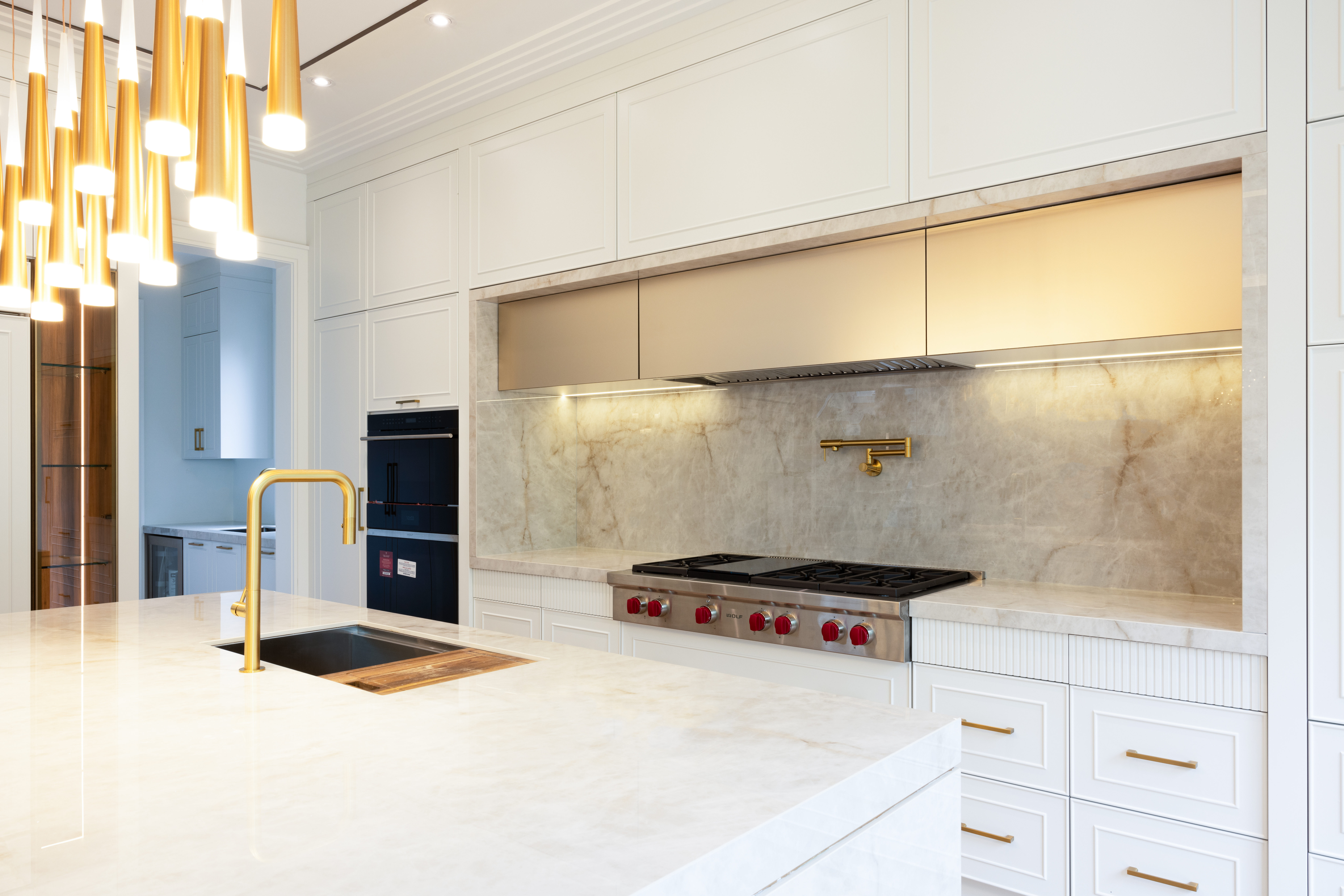 Bright kitchen with white cabinetry, stone countertops, gold fixtures, and professional range