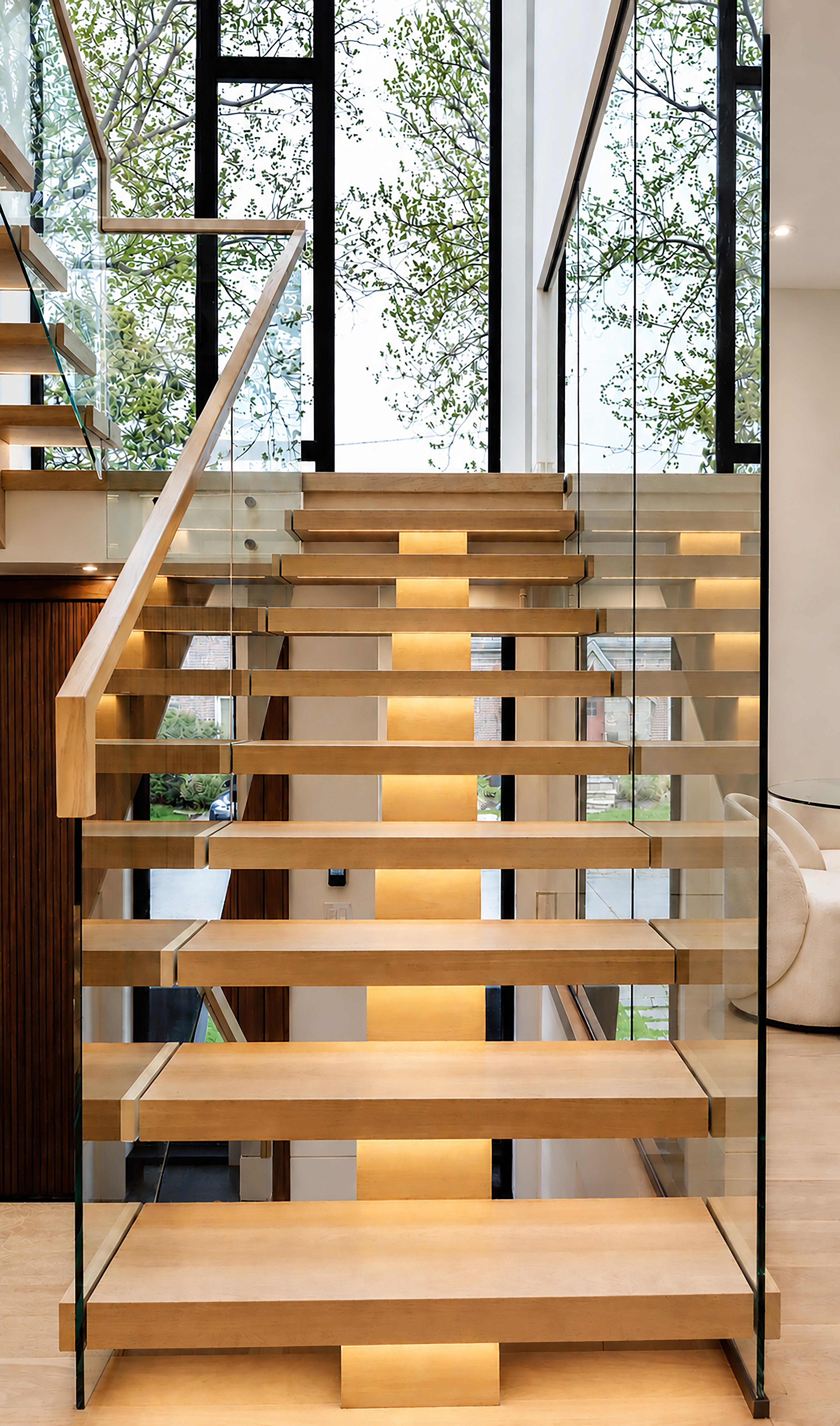 Close-up of floating wood staircase with glass railings and integrated lighting
