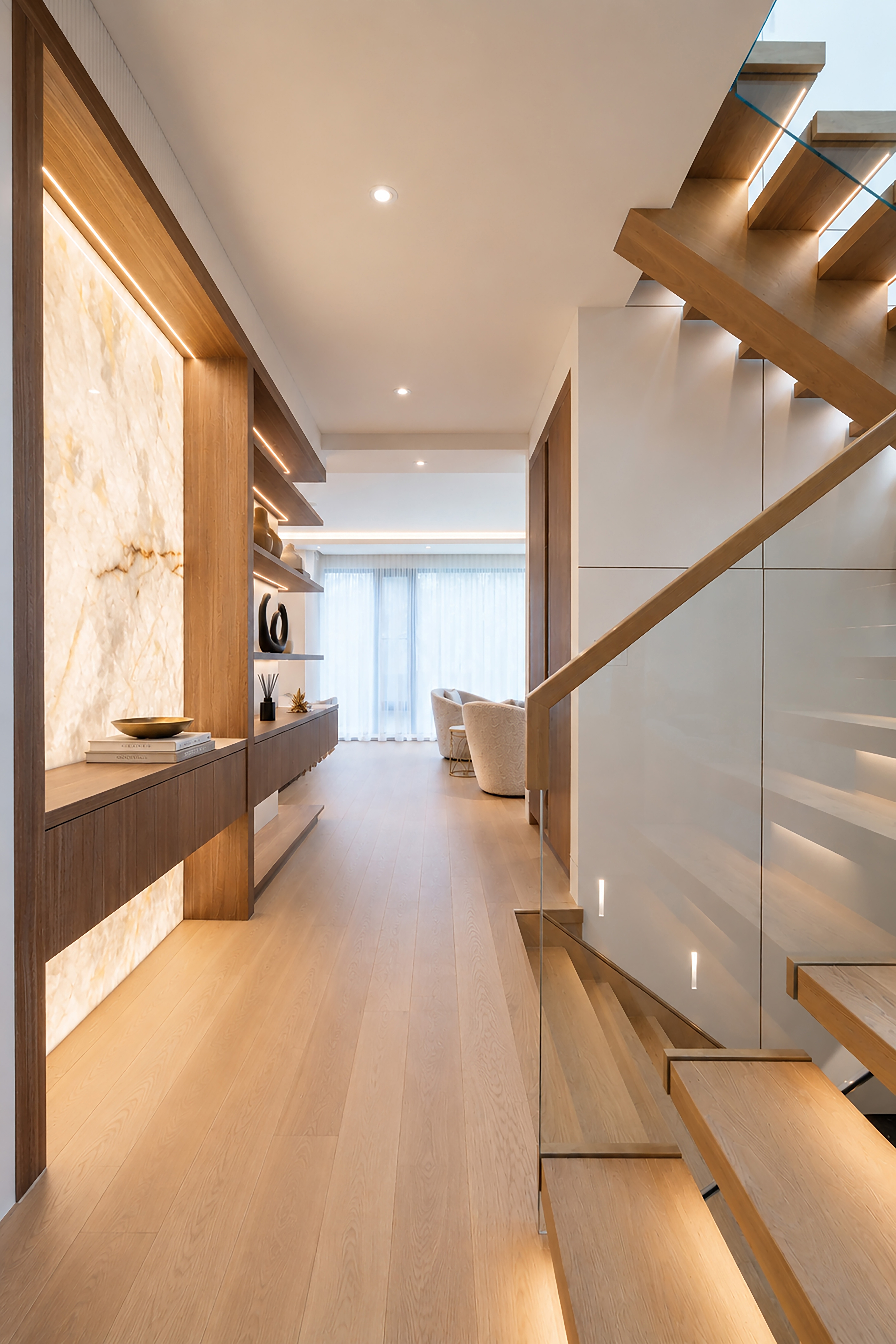 Hallway with backlit stone feature wall, wood cabinetry, and staircase