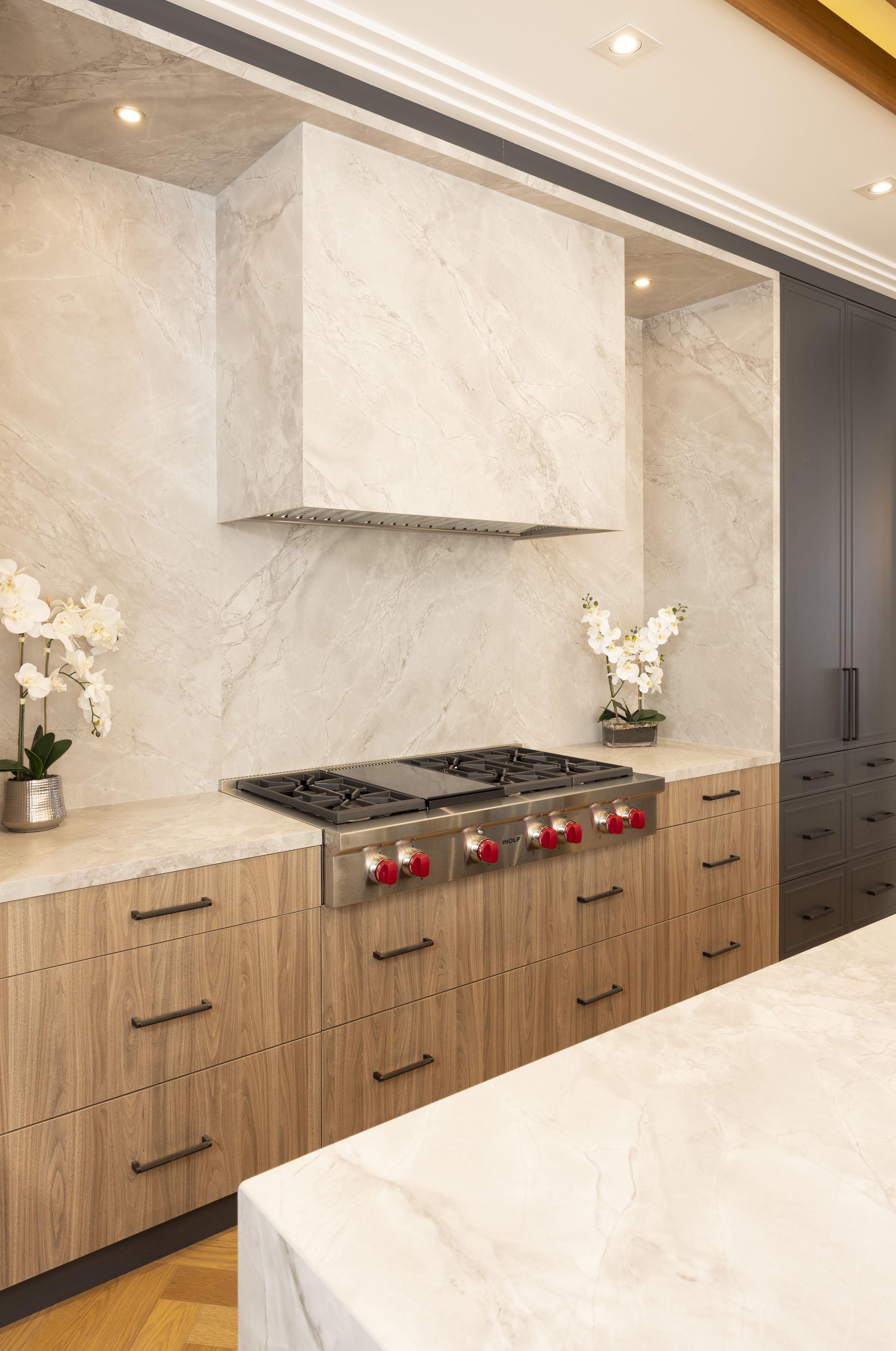 Light wood kitchen cabinetry with stone range hood, stone backsplash, and red stove knobs