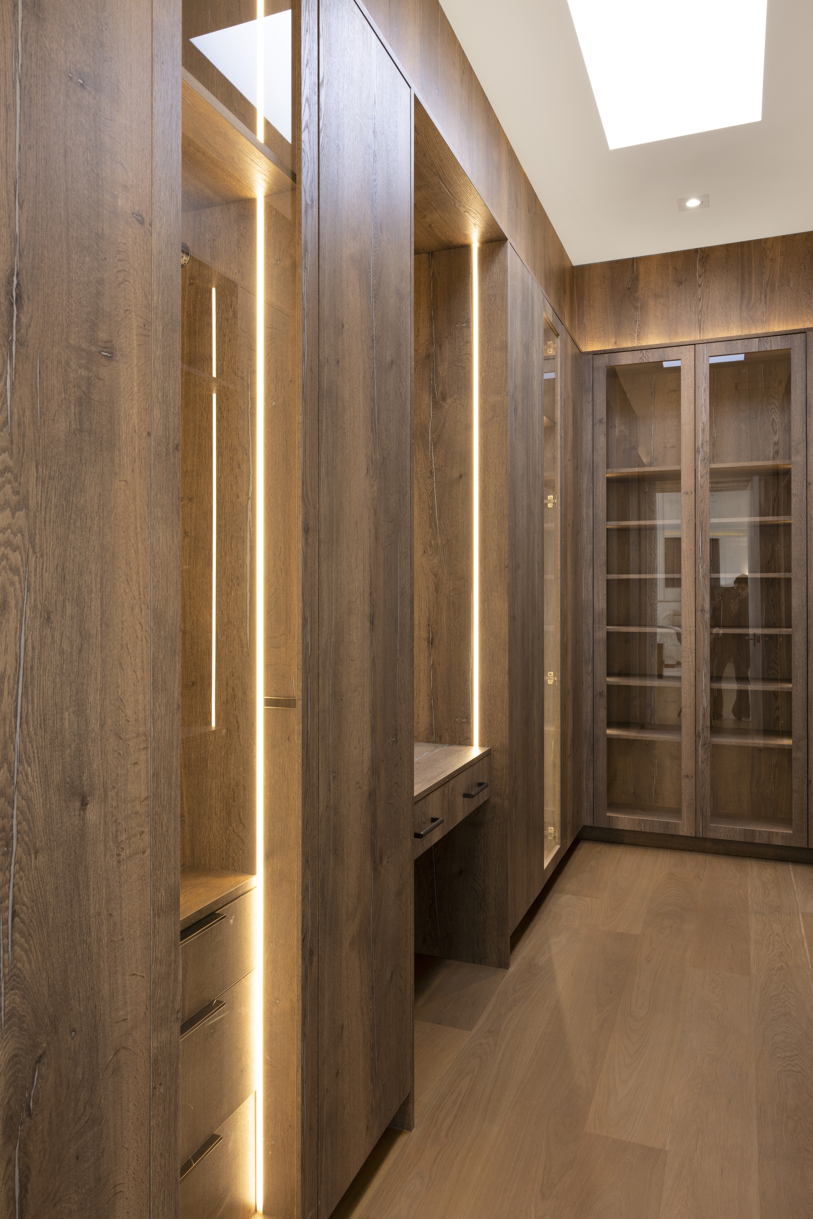 Dark wood walk-in closet with glass-front cabinetry and integrated vertical lighting