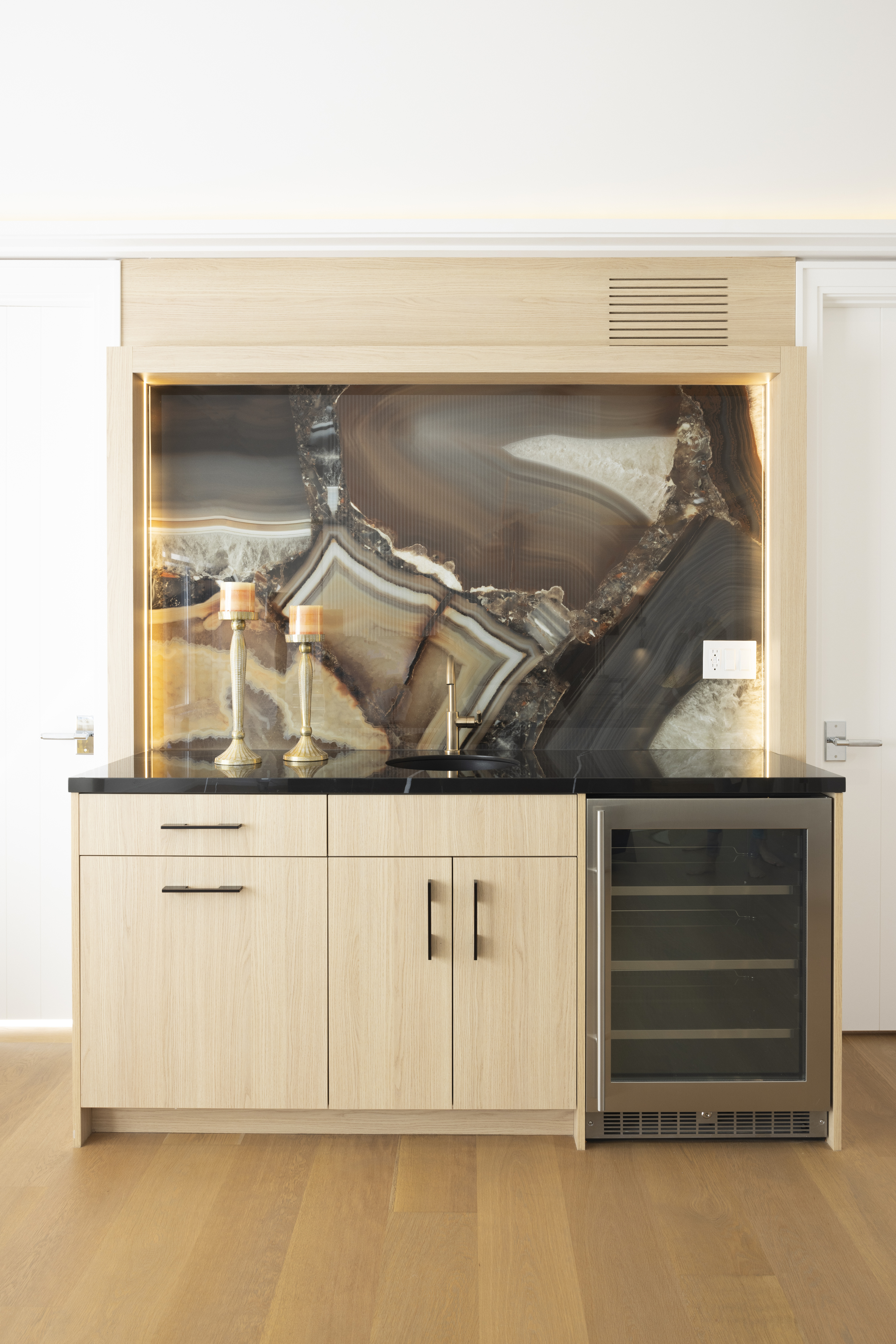 Custom home bar with light wood cabinetry, backlit stone backsplash, and beverage refrigerator