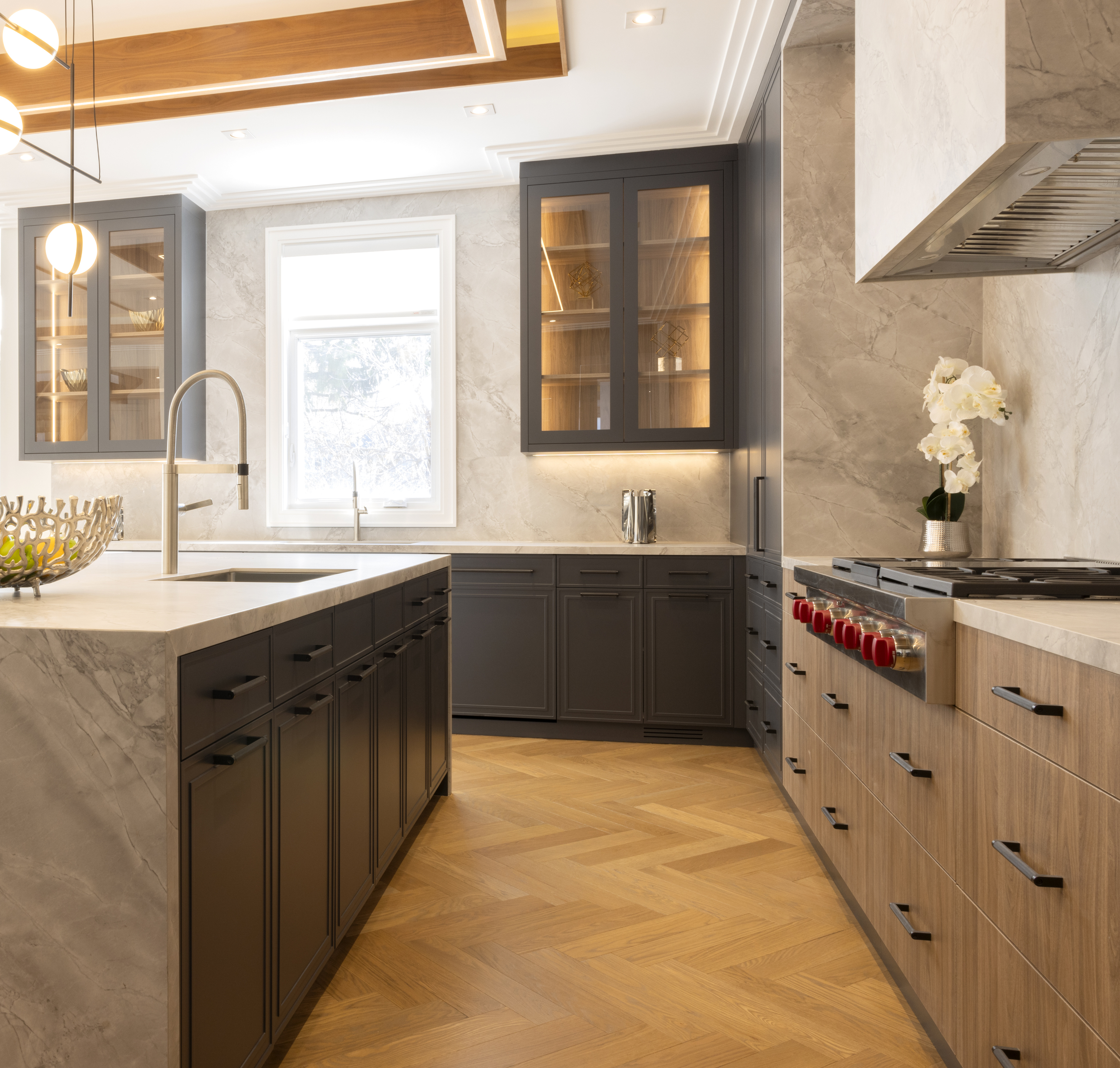 Modern kitchen with dark island, light wood cabinetry, stone surfaces, and large window
