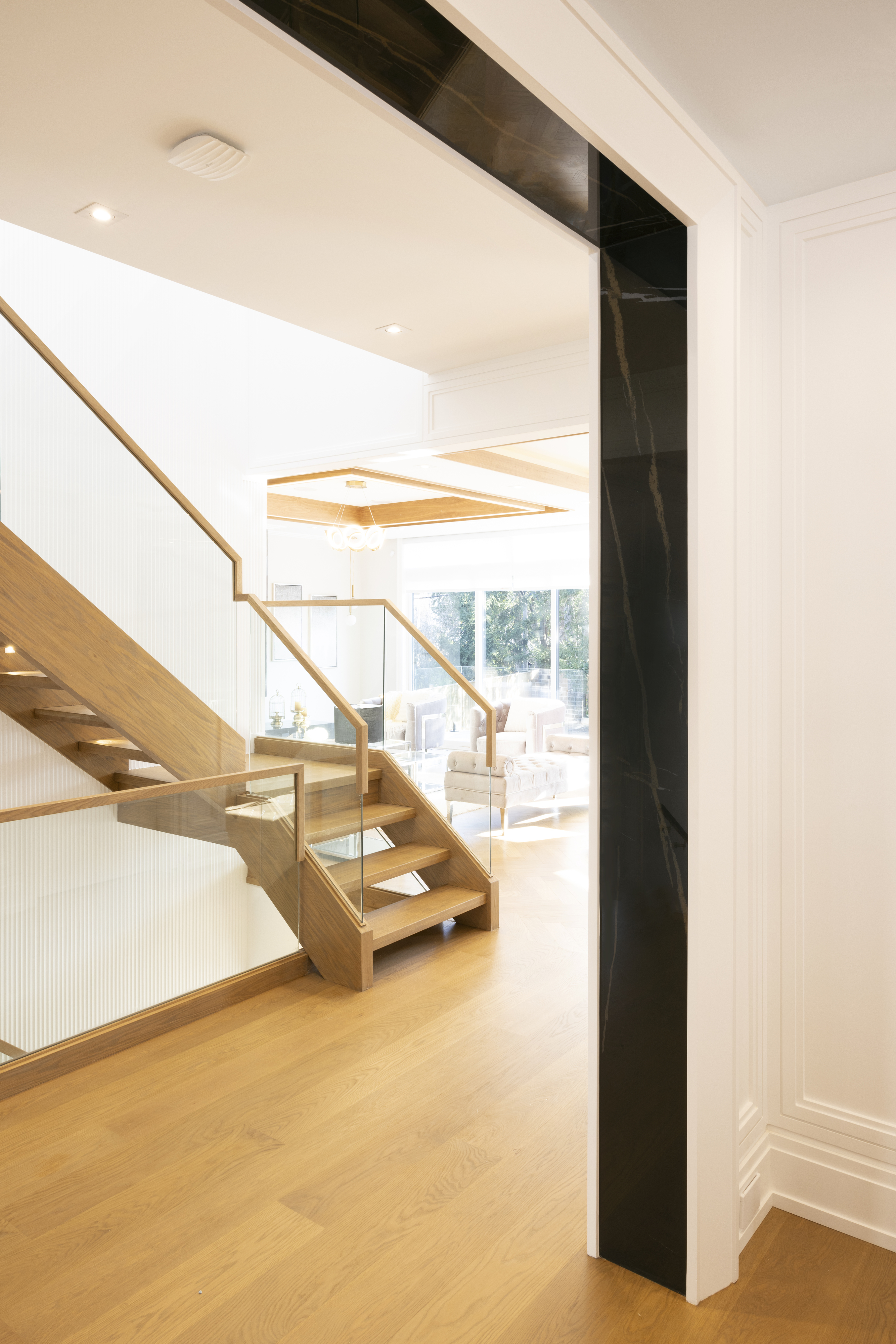 Open-riser wood staircase with glass railing beside a dark stone feature wall