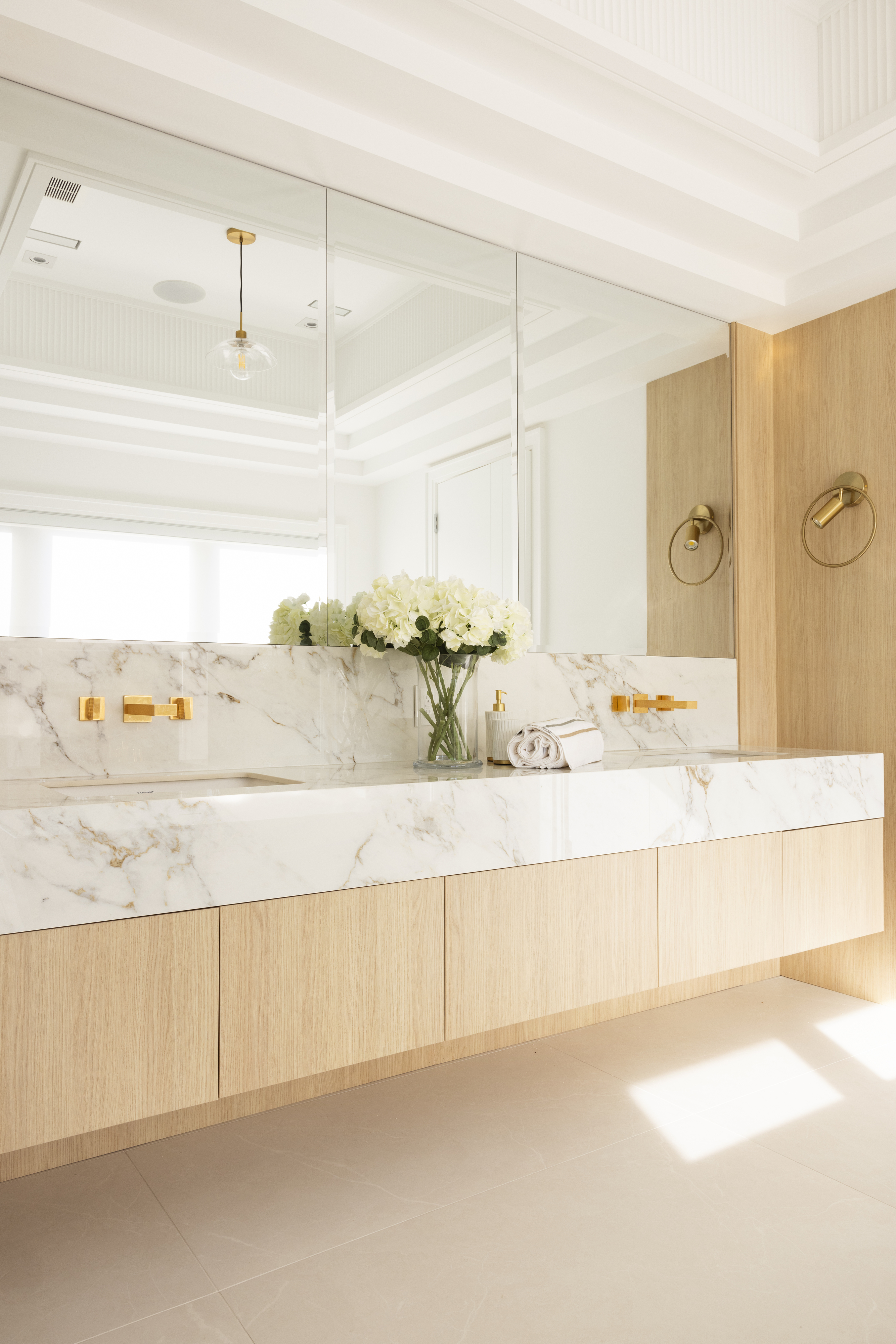 Bright bathroom with marble double vanity, light wood cabinetry, and gold fixtures