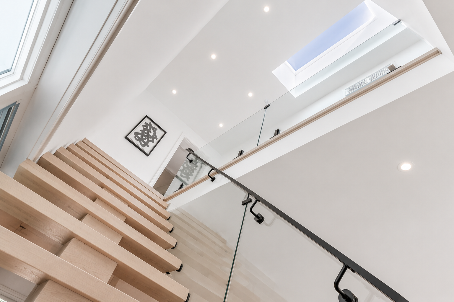 Open wood staircase with glass railing, skylight, and recessed ceiling lights