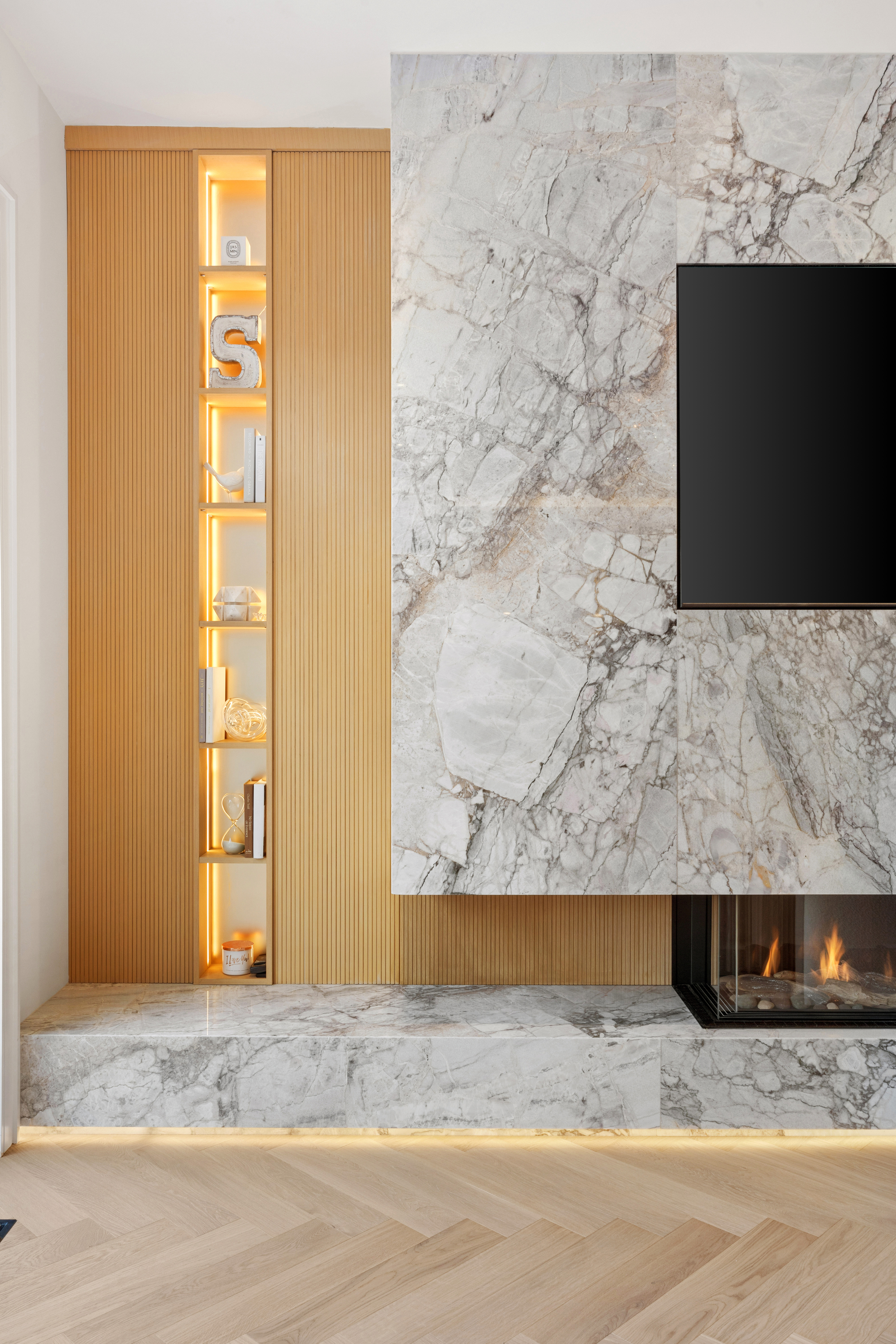 Close-up of stone television wall with fireplace, wood slat panelling, and illuminated display niche