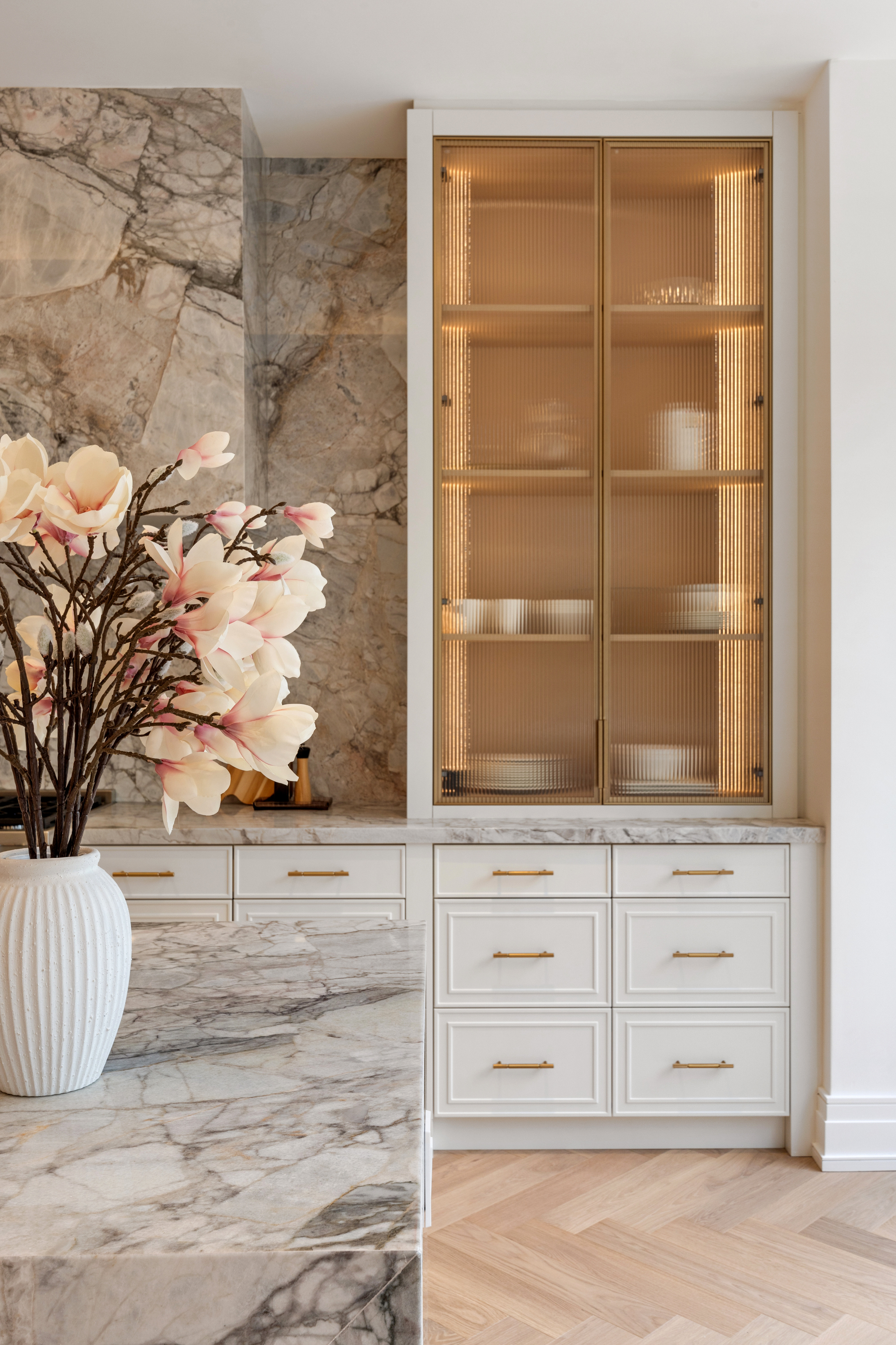 Close-up of kitchen cabinetry with ribbed glass doors, stone backsplash, and white drawers