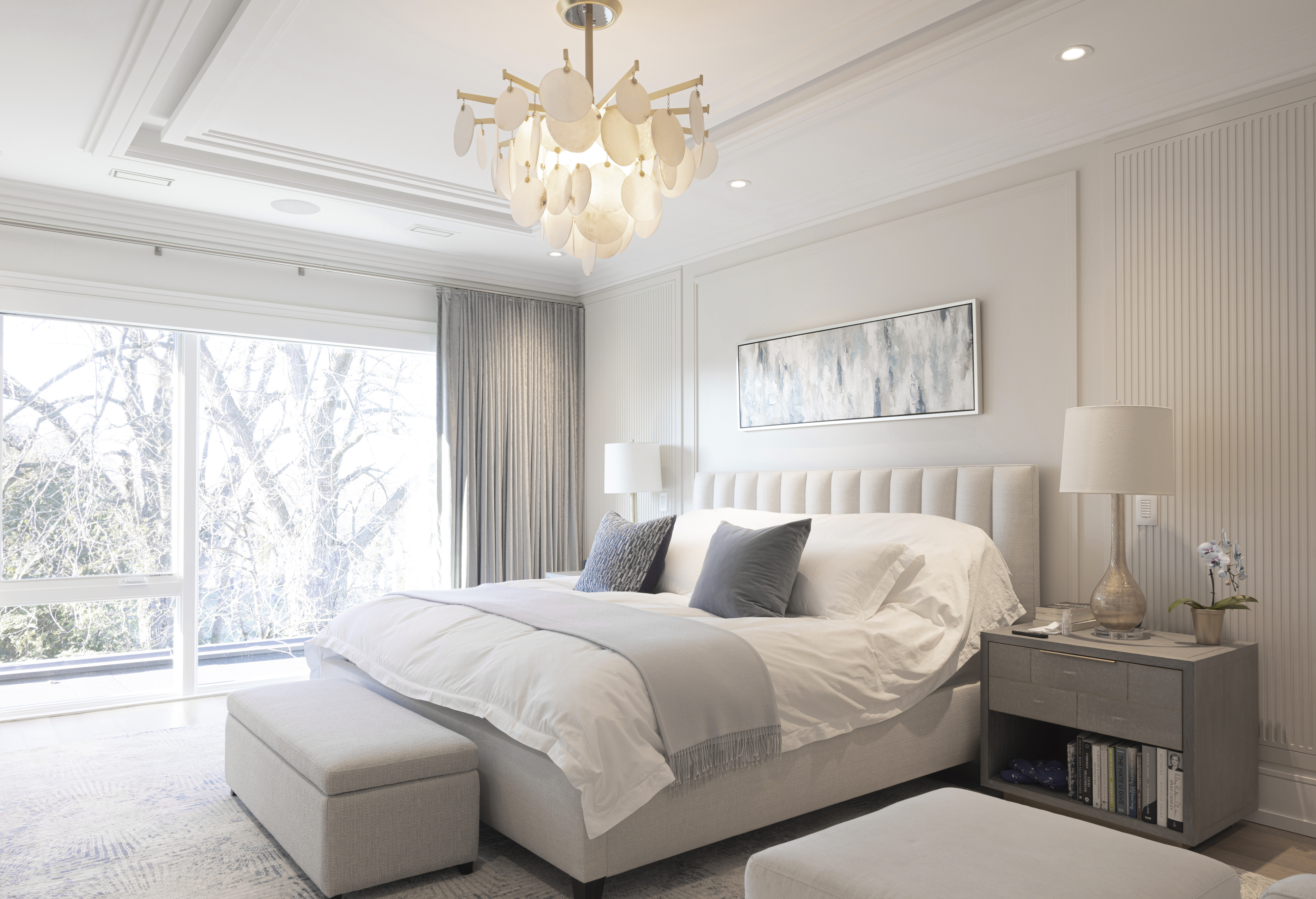 Spacious primary bedroom with upholstered bed, chandelier, neutral decor, and large window