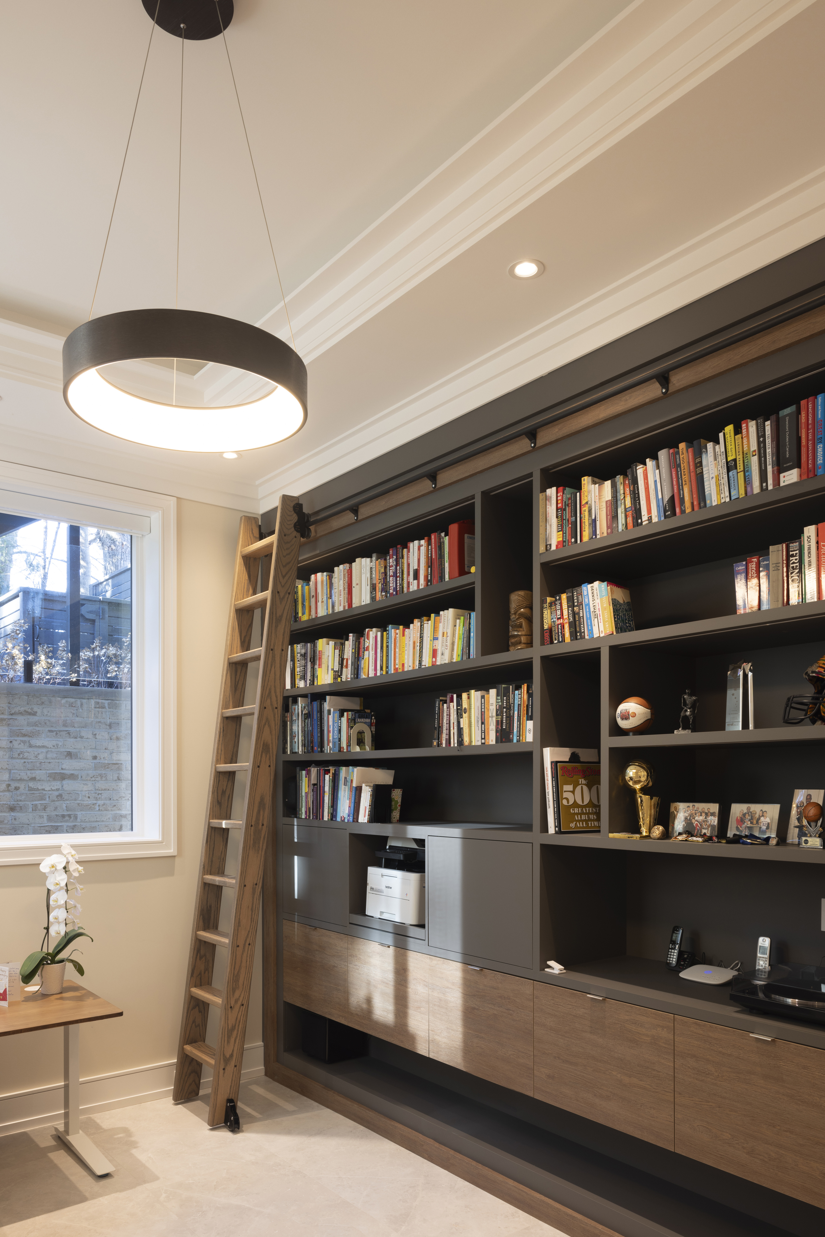 Home library with floor-to-ceiling black bookshelves, rolling ladder, and circular ceiling light