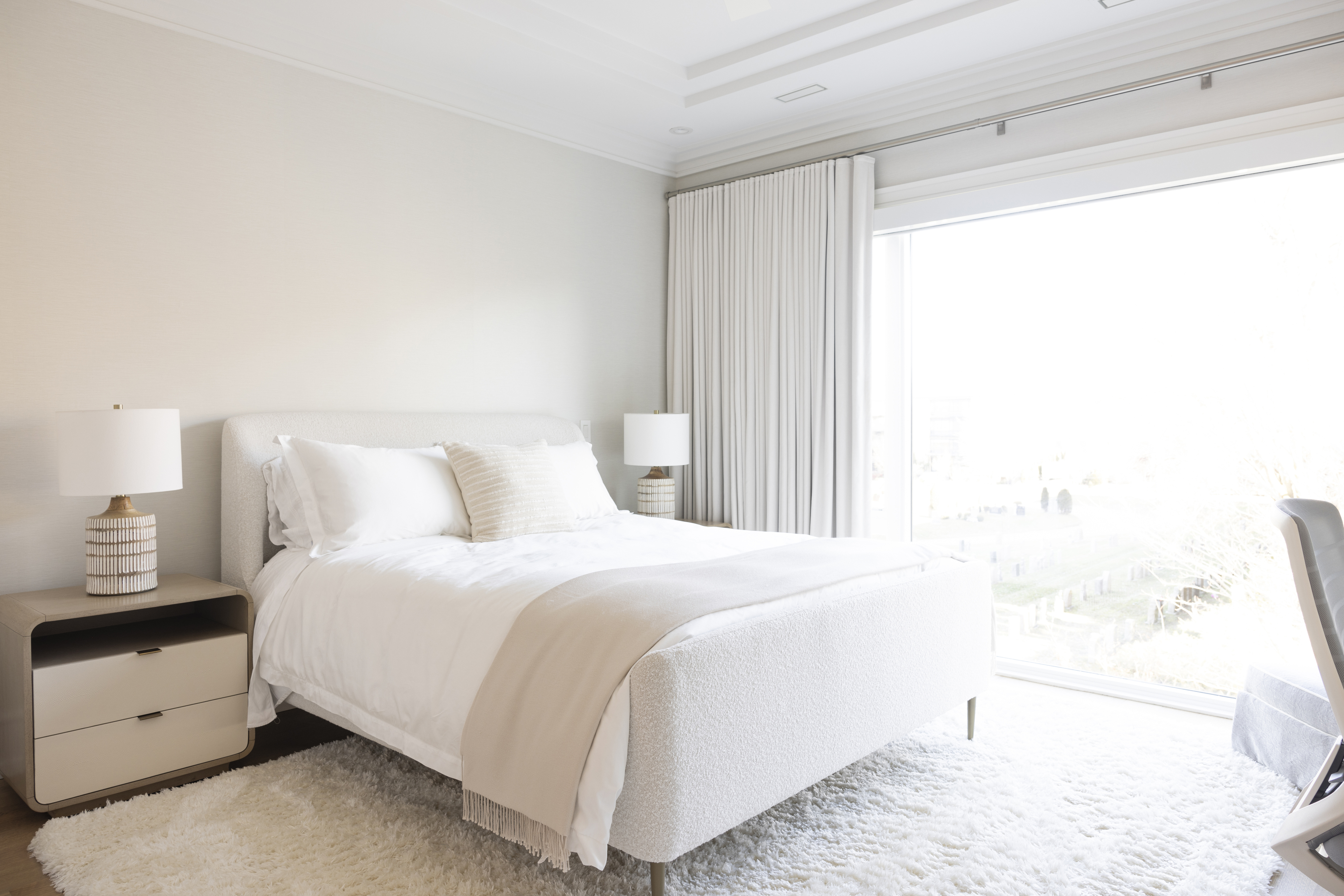 Bright bedroom with upholstered bed, neutral furnishings, and large window