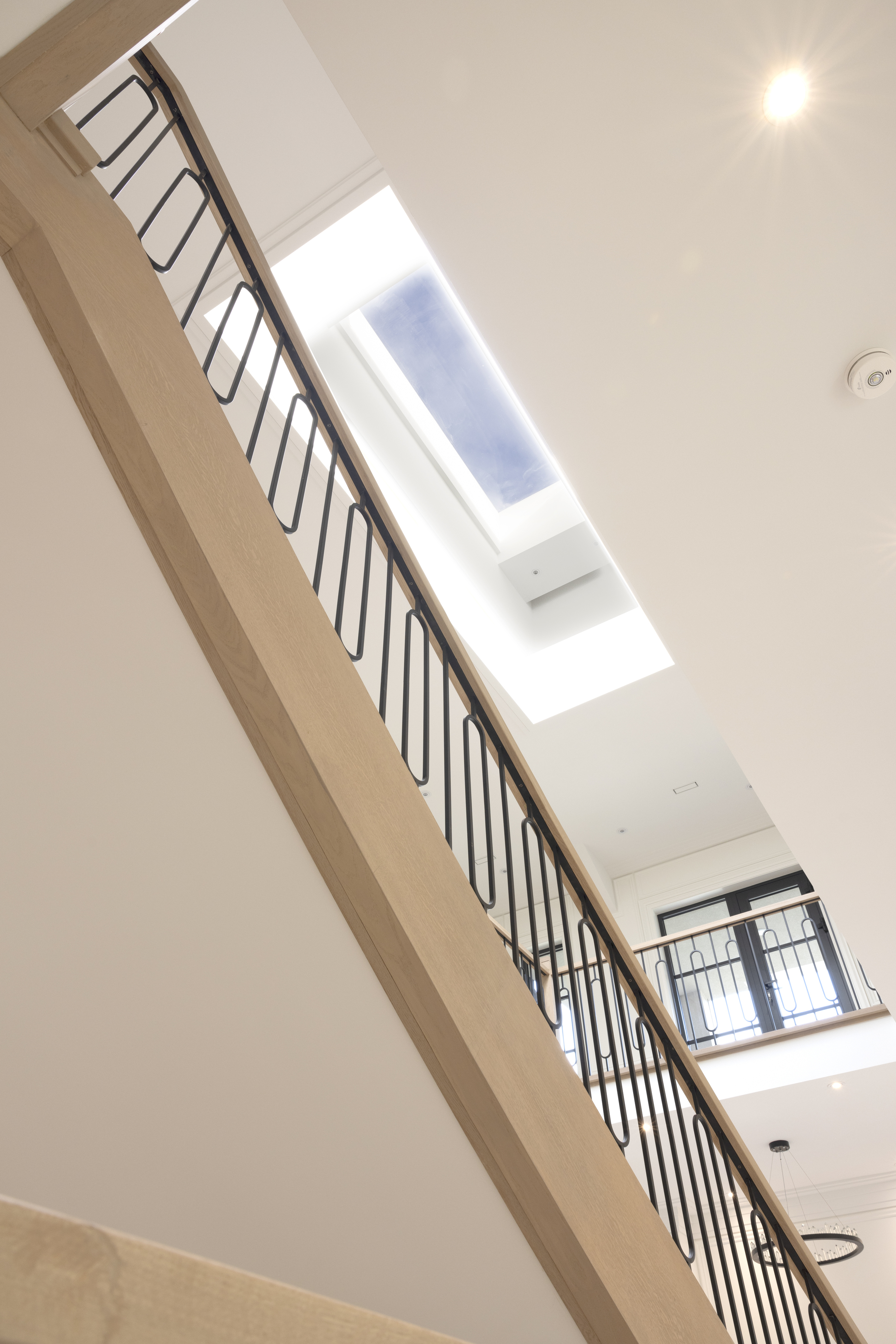 Staircase with black metal railing beneath a large ceiling skylight