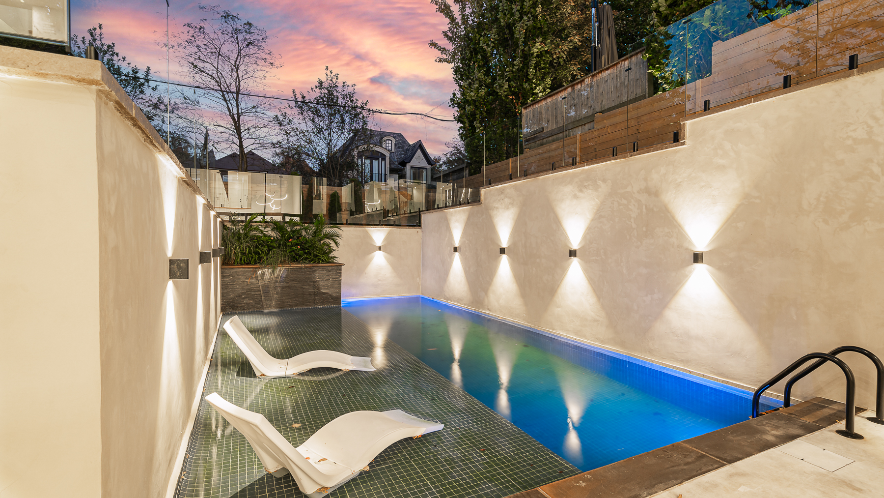 Outdoor swimming pool at dusk with submerged lounge chairs and dramatic wall lighting