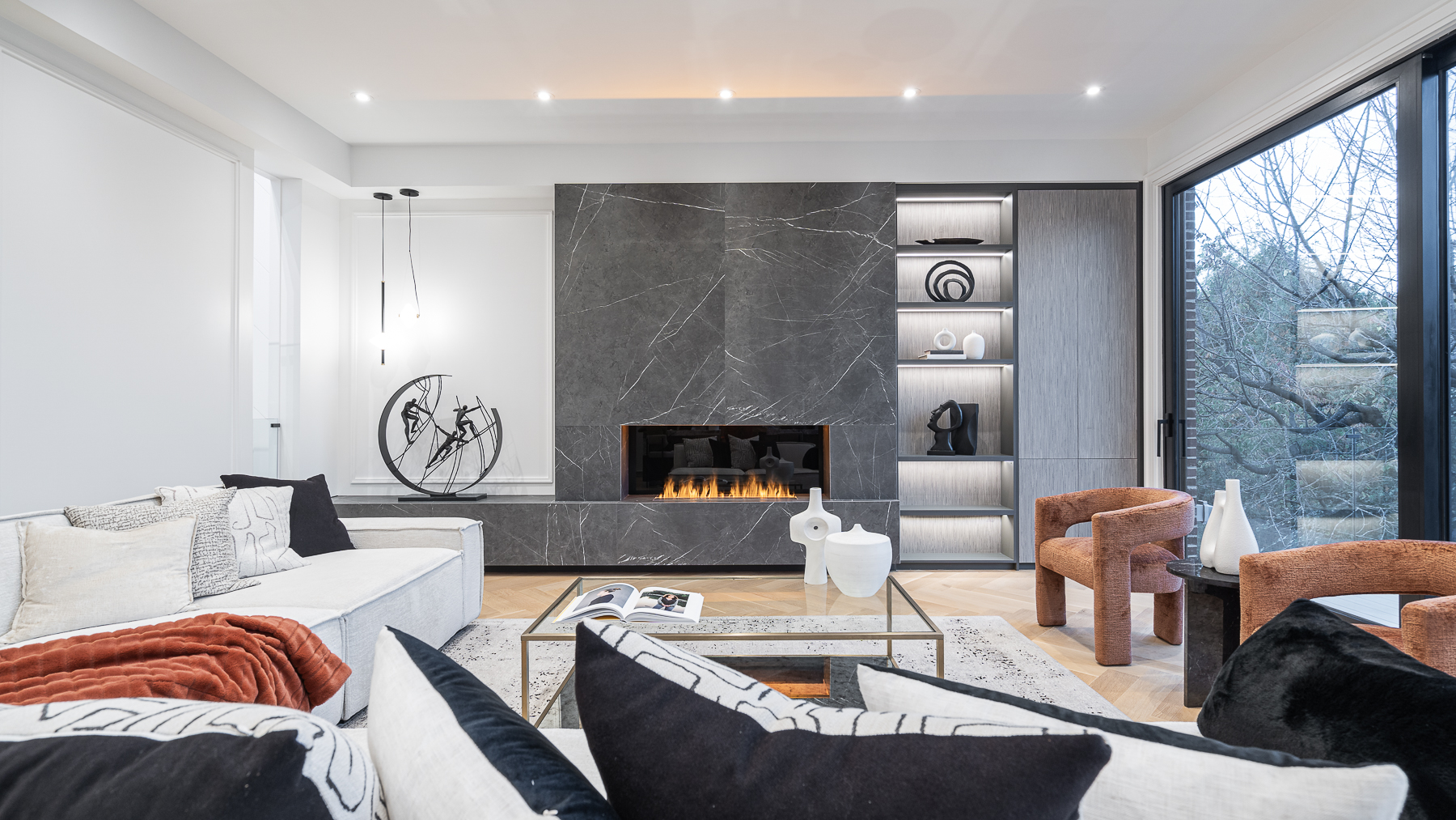 Contemporary living room with dark stone fireplace, white seating, and illuminated shelving