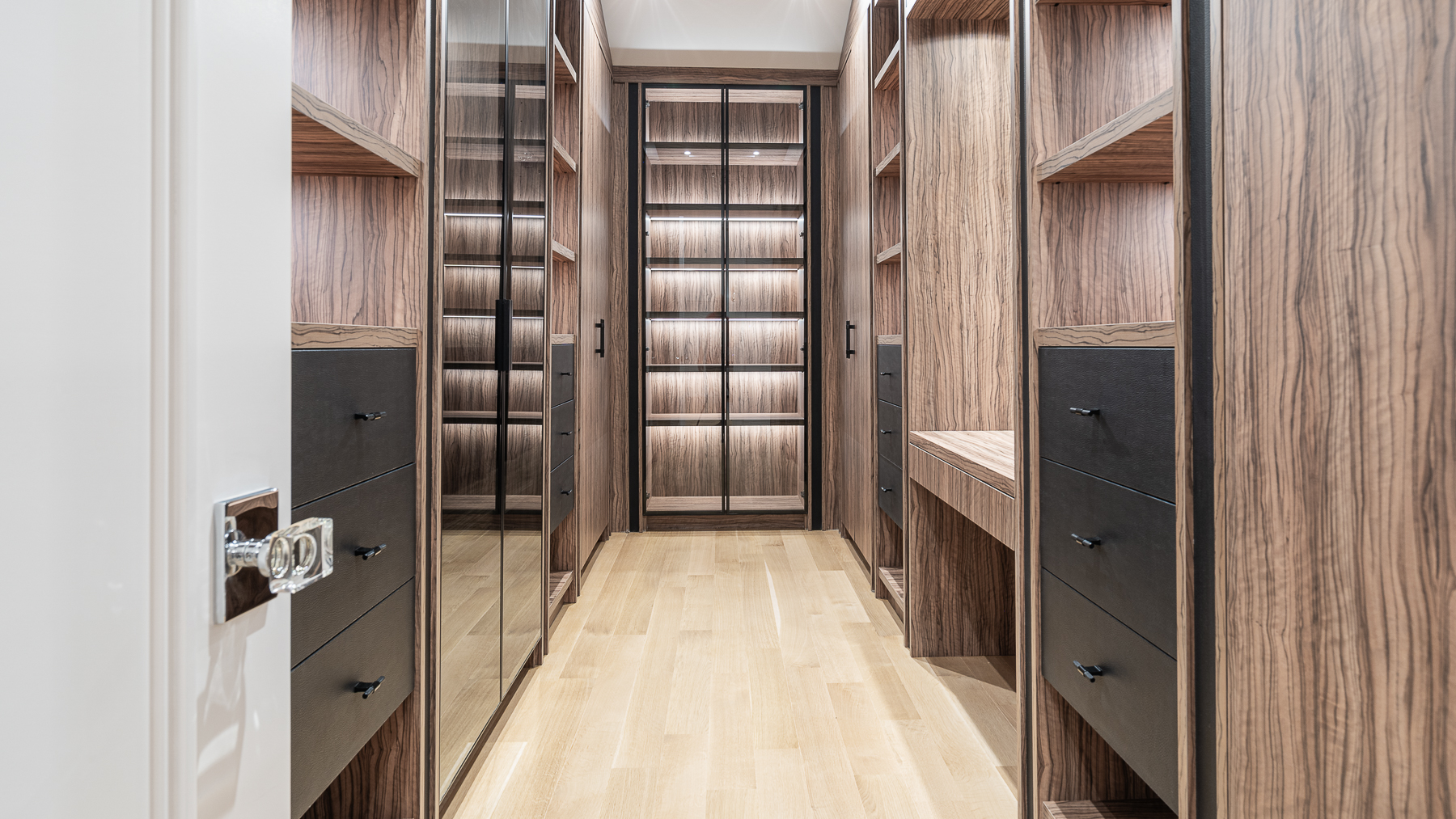 Walk-in closet with wood cabinetry, glass-front storage, drawers, and integrated lighting