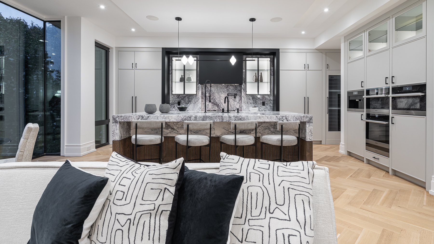 Open kitchen with marble island, black accents, pendant lights, and adjoining living area