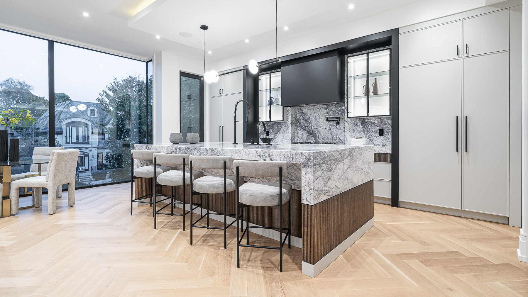 Modern kitchen with marble island, dark wood base, bar stools, and large windows