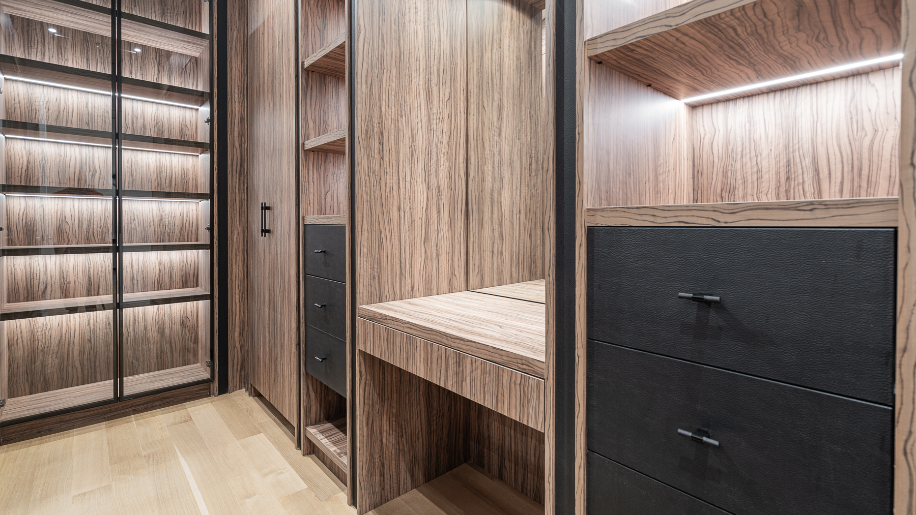 Close-up of custom wood walk-in closet cabinetry with drawers and illuminated shelving