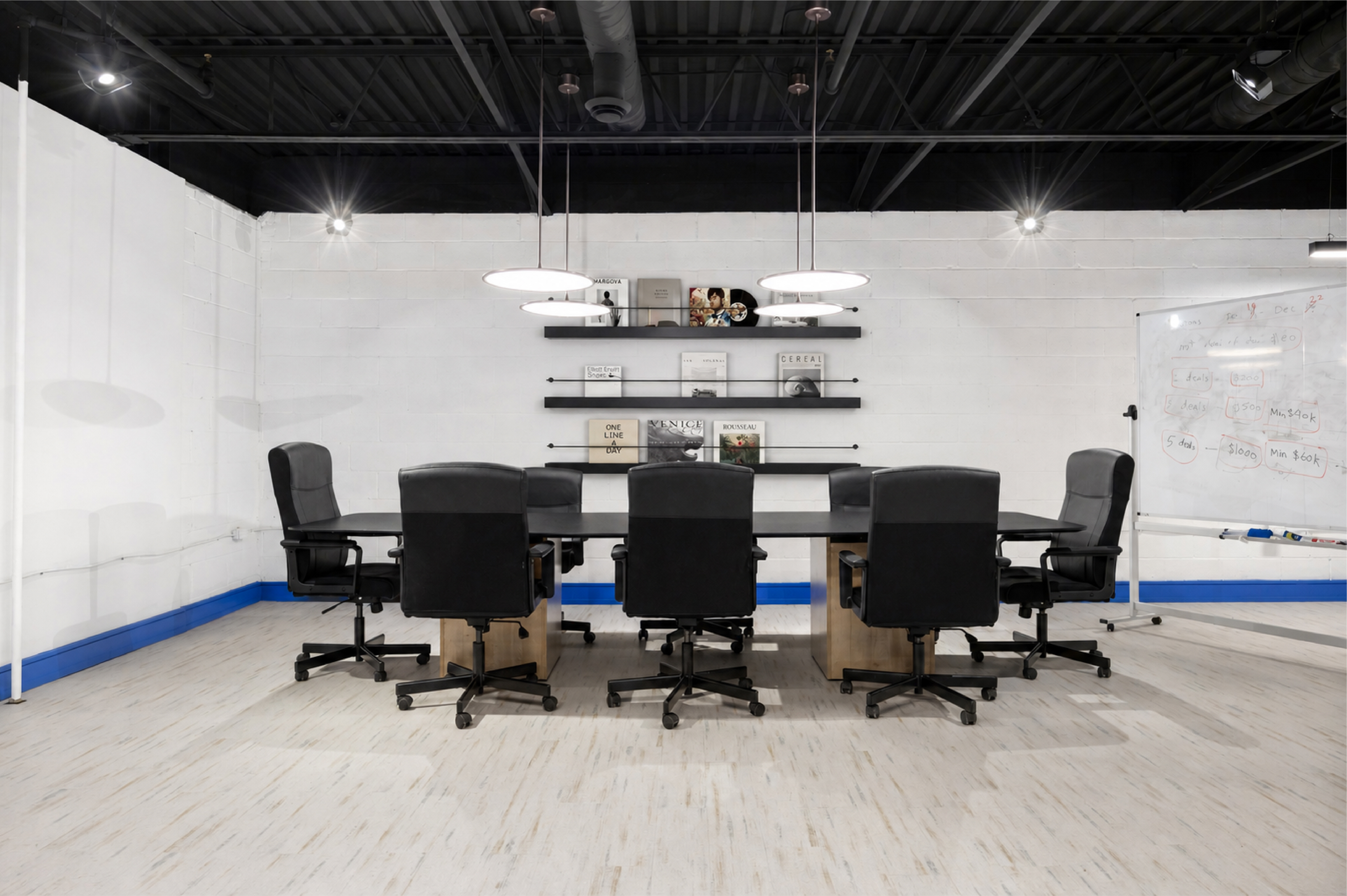 Modern conference room with black chairs, large table, pendant lights, and wall shelving