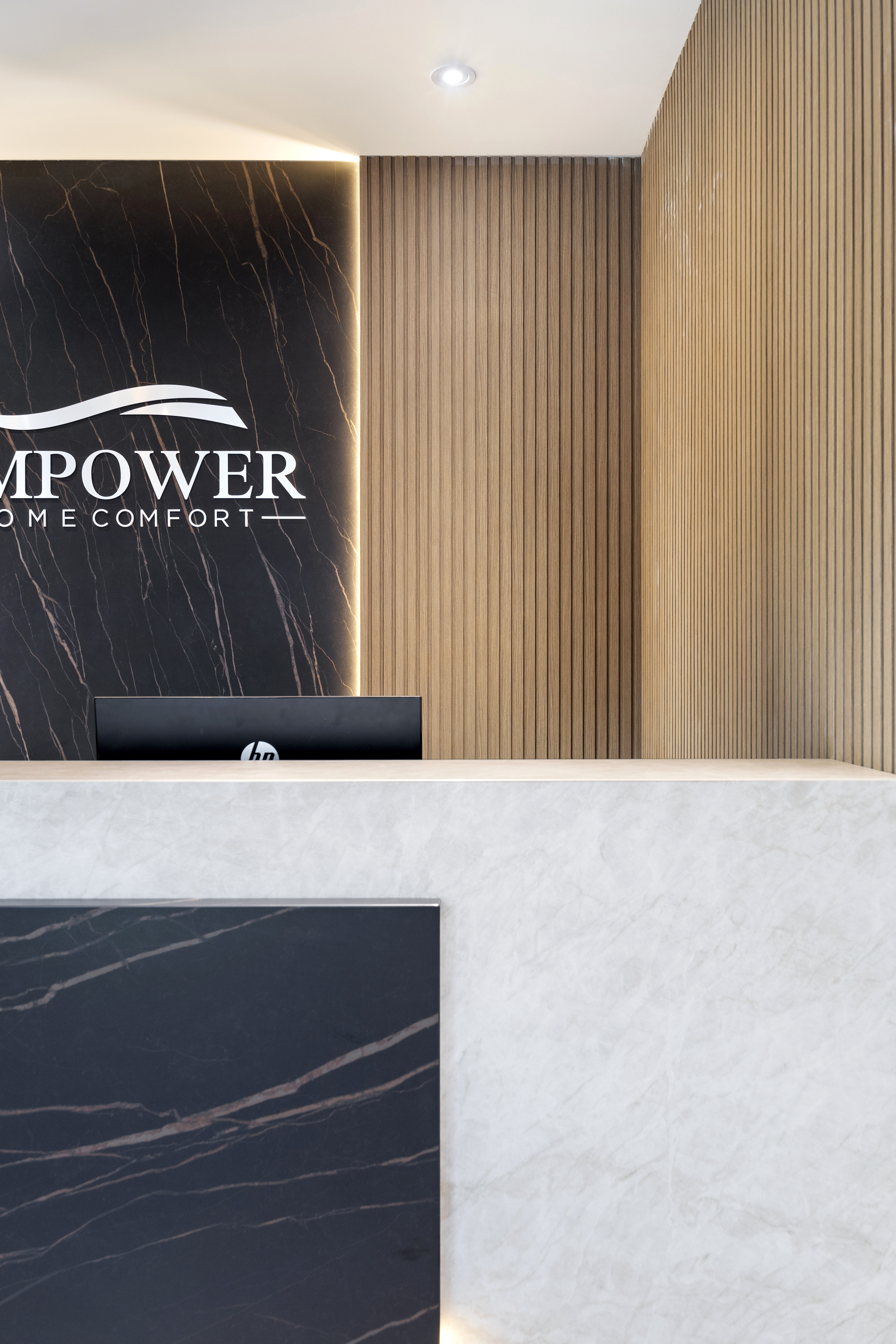 Close-up of office reception desk with marble counter, black stone backdrop, and wood slat wall