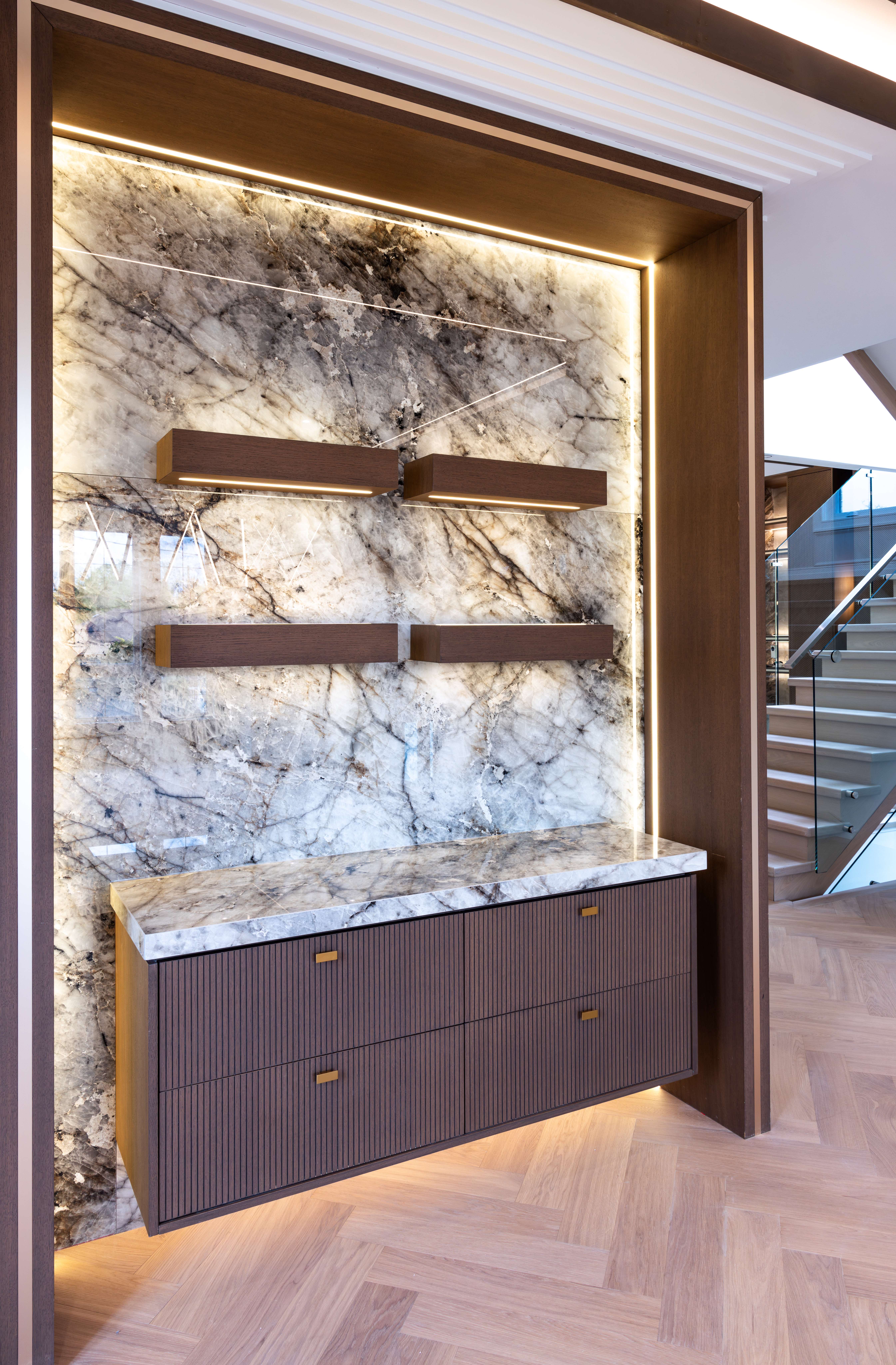 Backlit stone feature wall with floating dark wood shelves and custom cabinetry