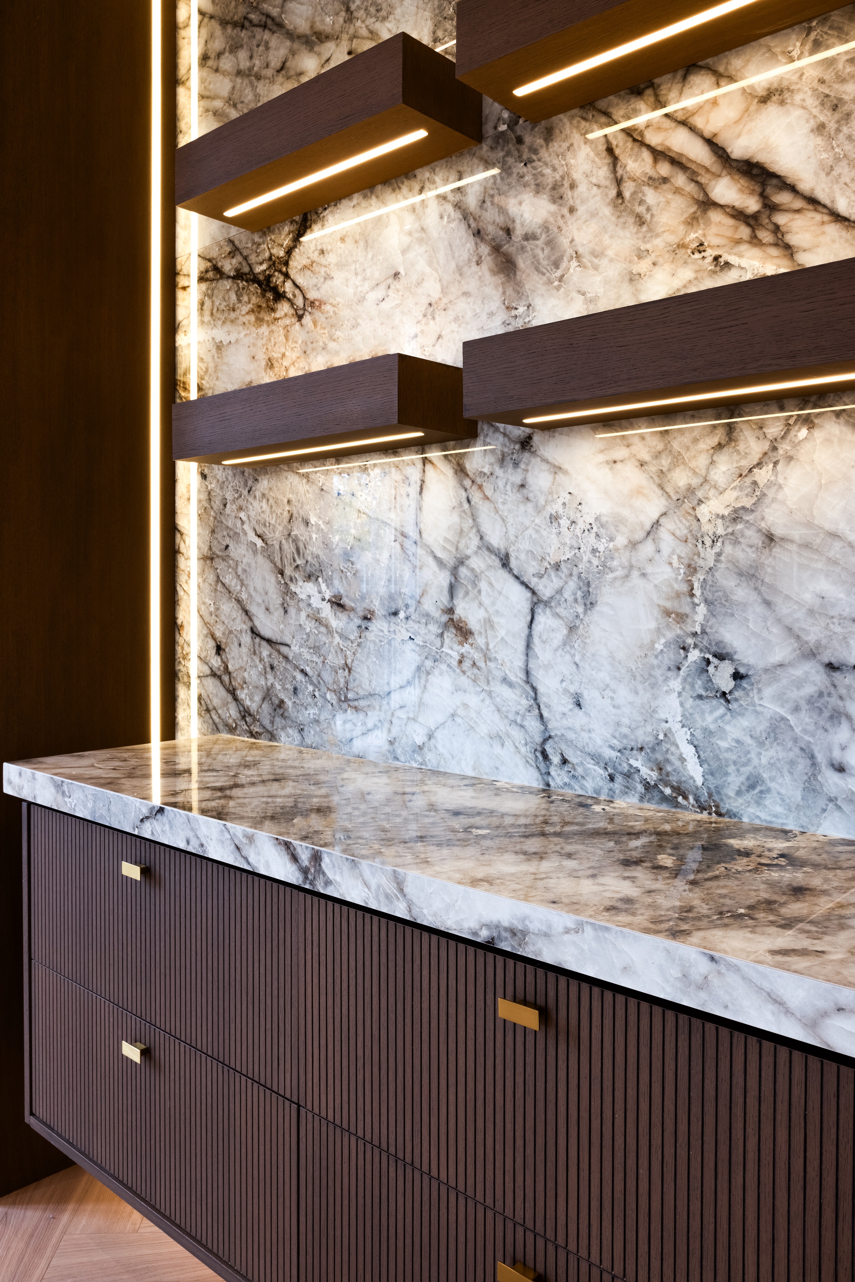 Close-up of illuminated stone backsplash with floating dark wood shelves