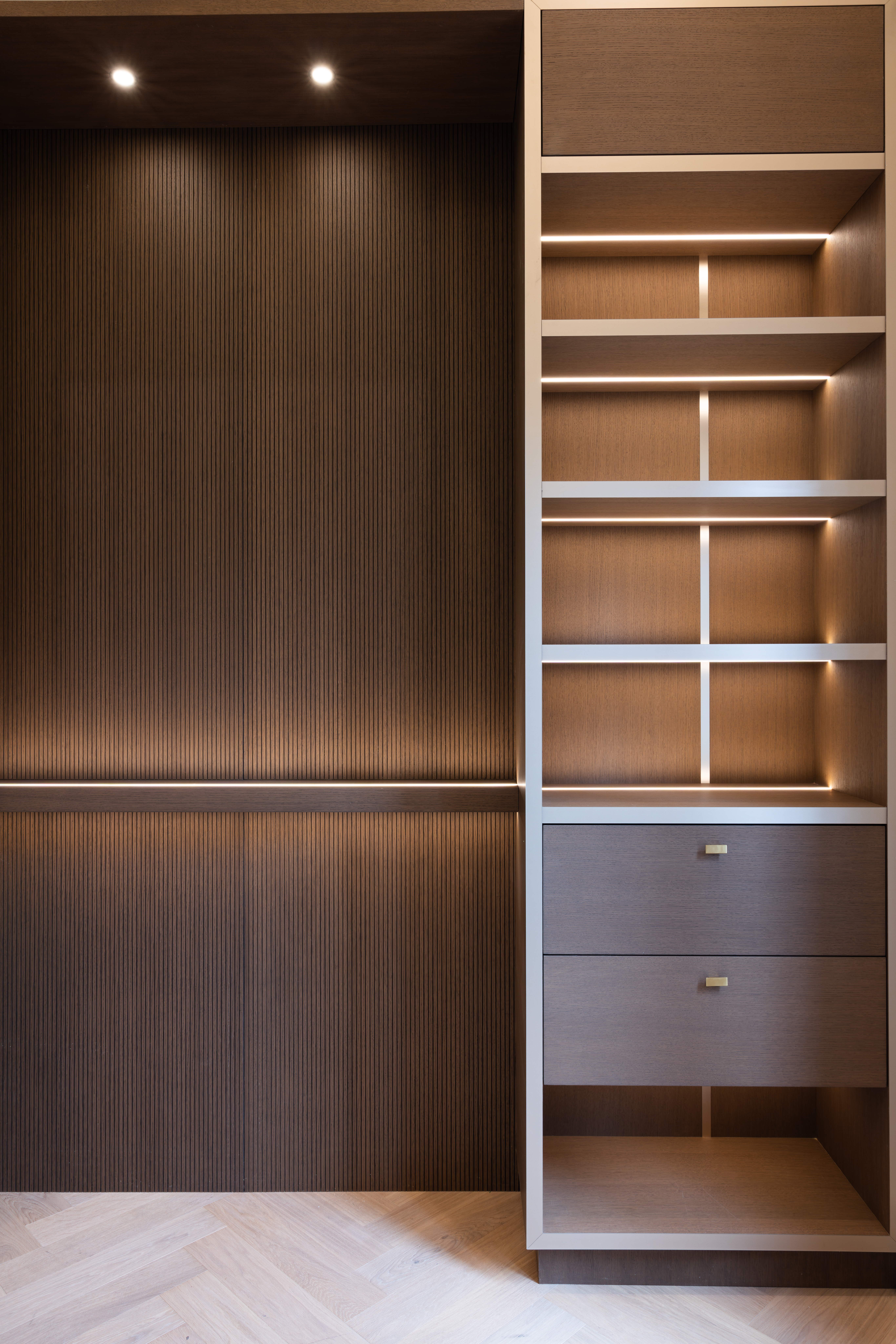Close-up of dark wood shelving, fluted wall panels, and illuminated display niches