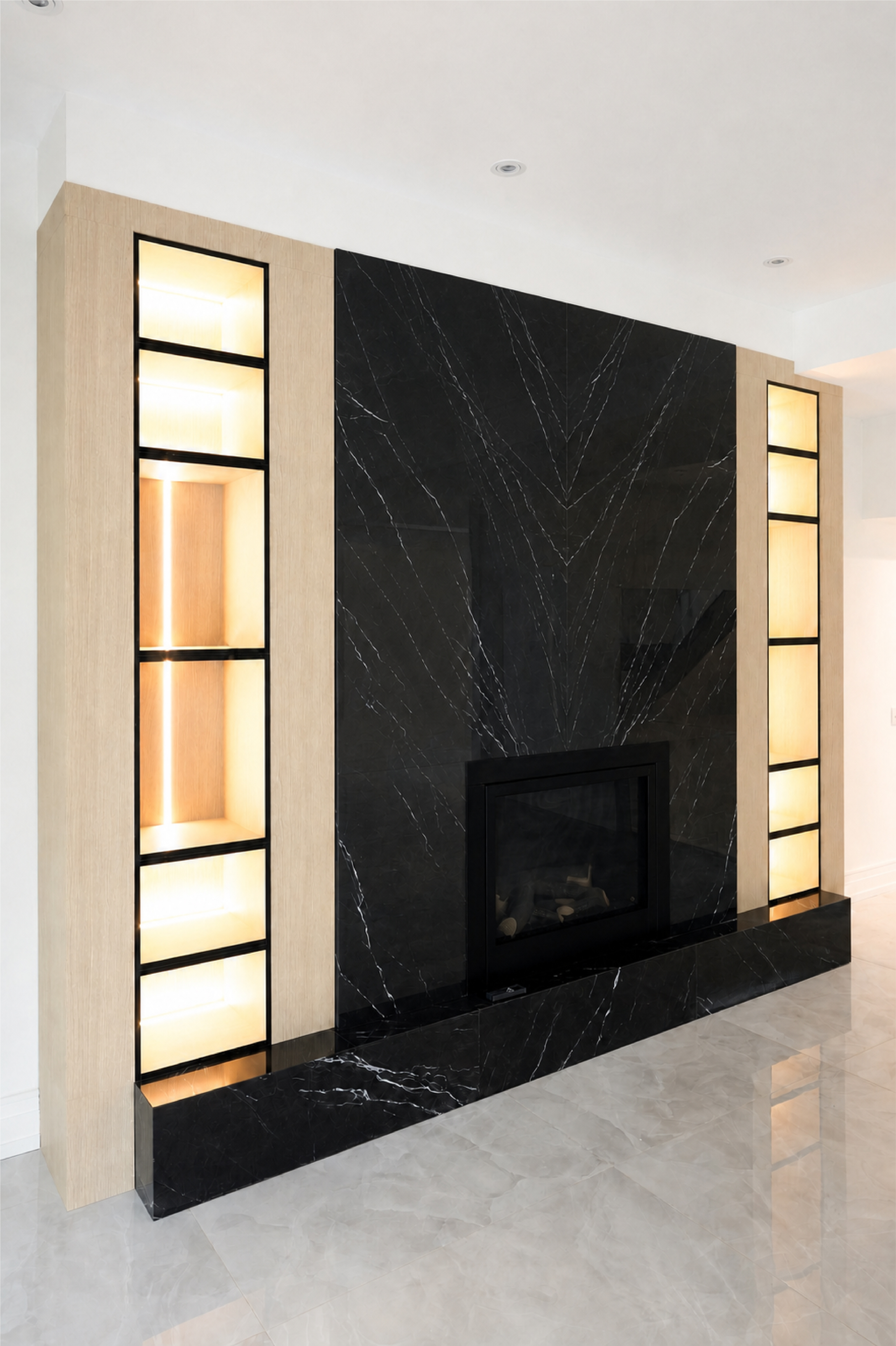 Black stone fireplace framed by illuminated display niches and light wood panelling