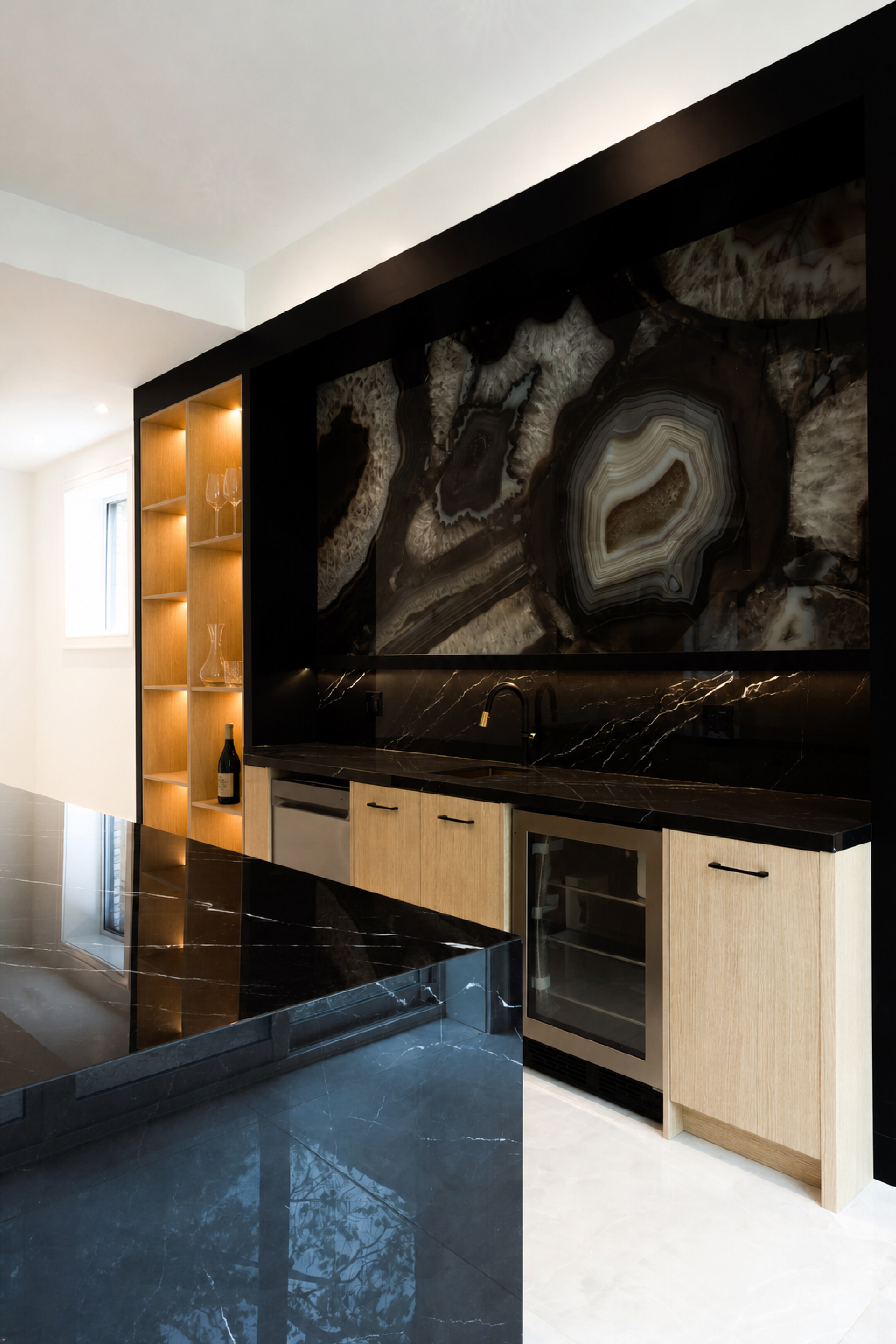 Close-up of home bar with backlit stone feature wall, dark countertop, and beverage refrigerator