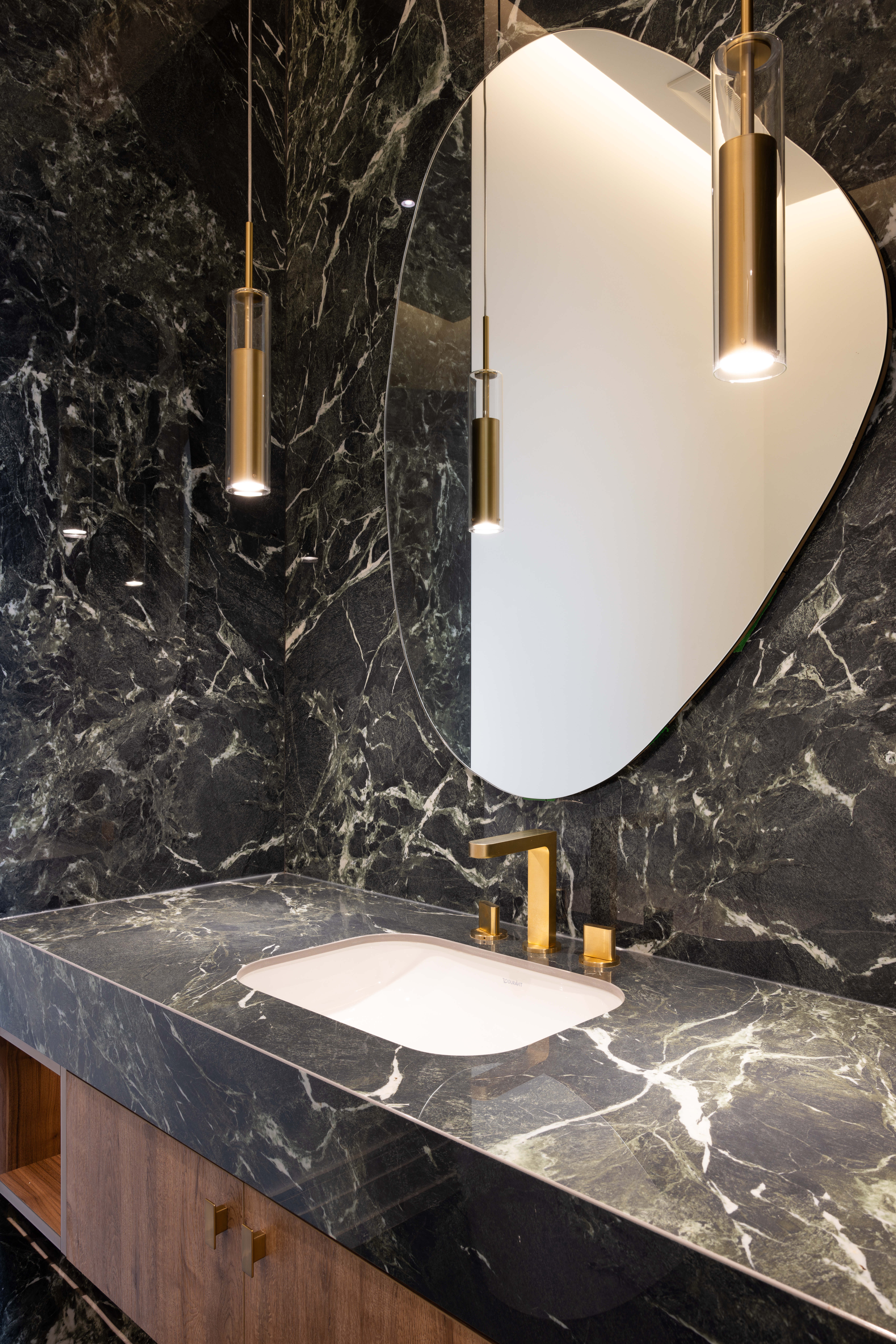 Powder room with black marble vanity, curved mirror, pendant lights, and gold fixtures