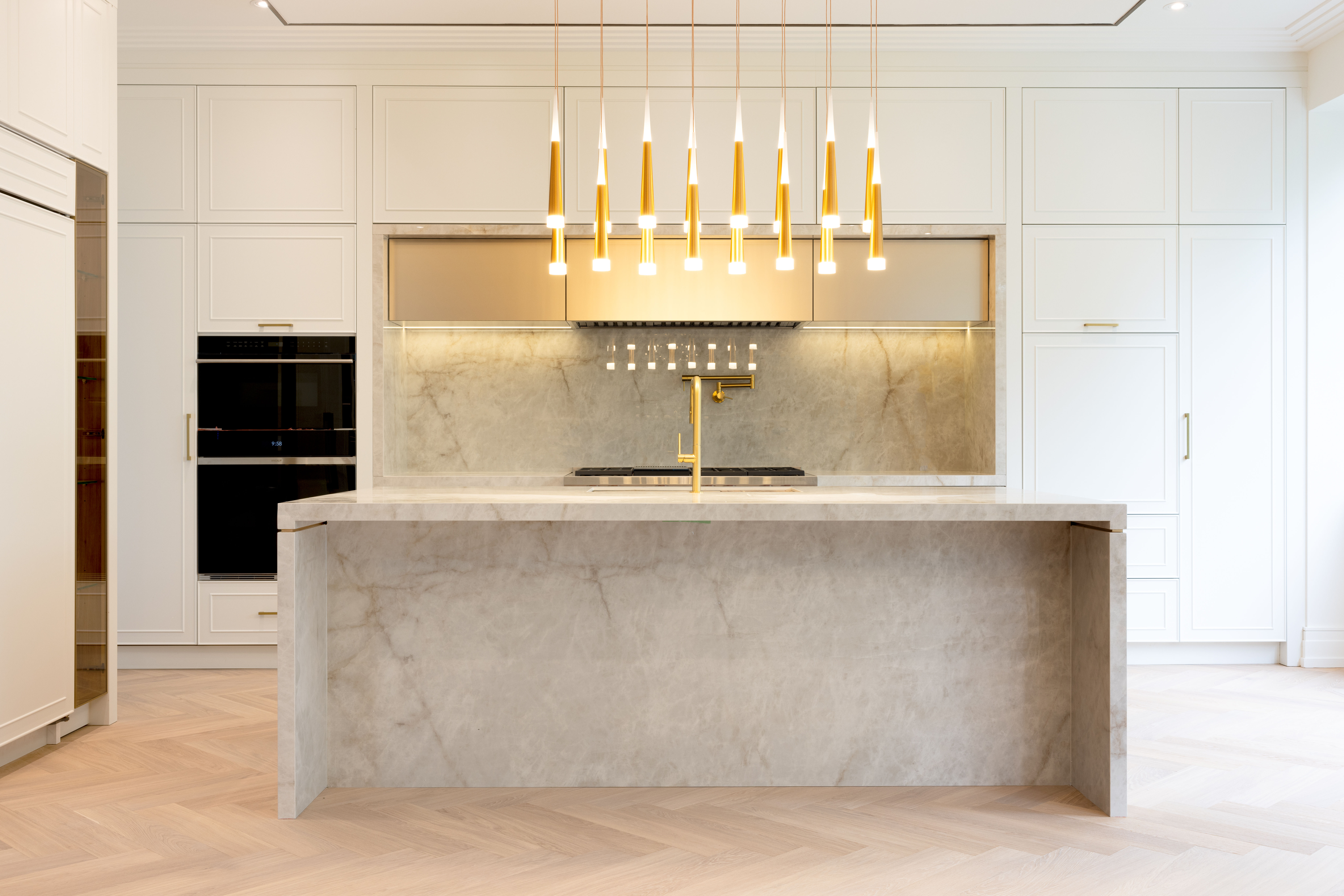 White kitchen with stone island, gold pendant lights, and floor-to-ceiling cabinetry