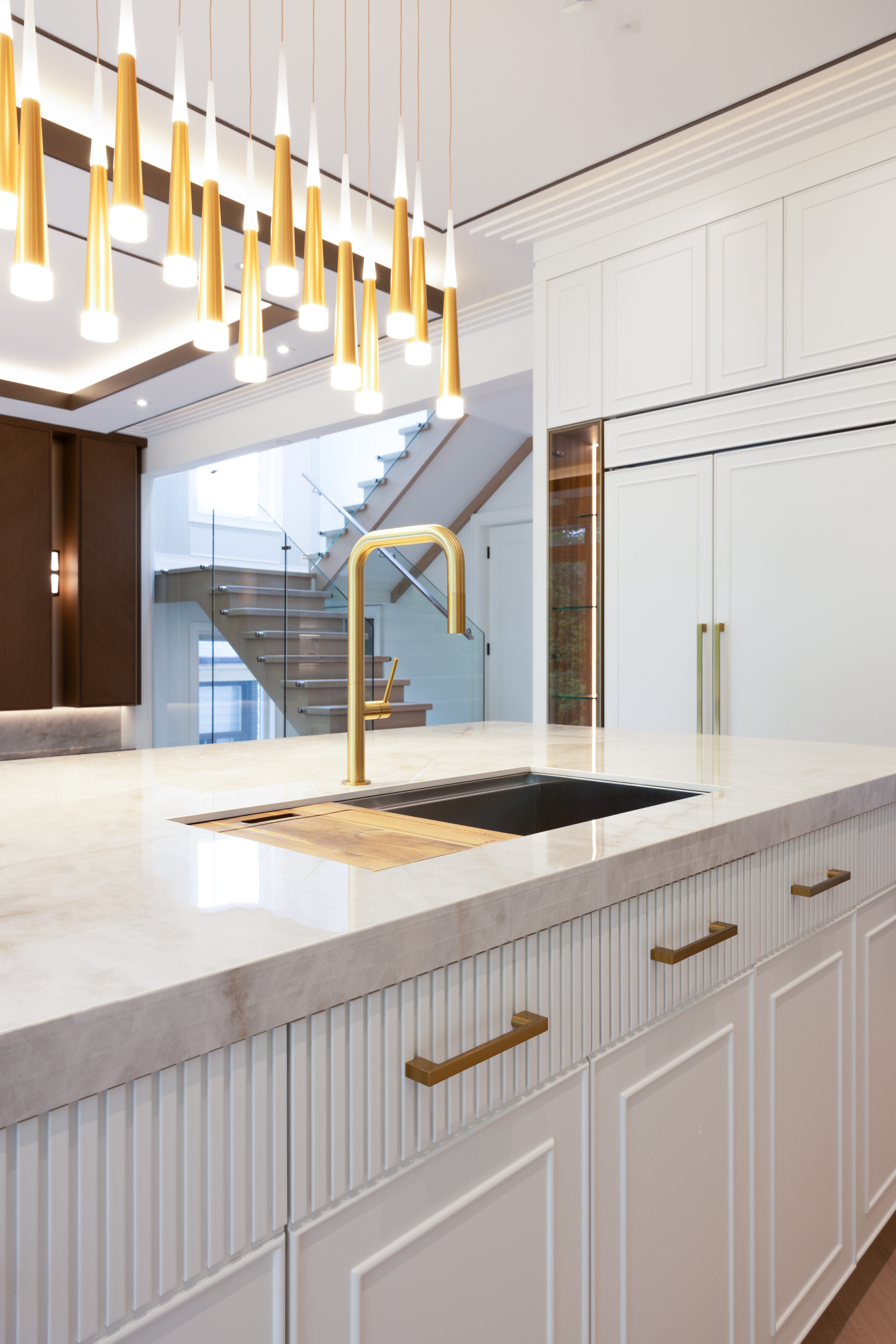 Close-up of stone kitchen island with gold faucet and open staircase in the background