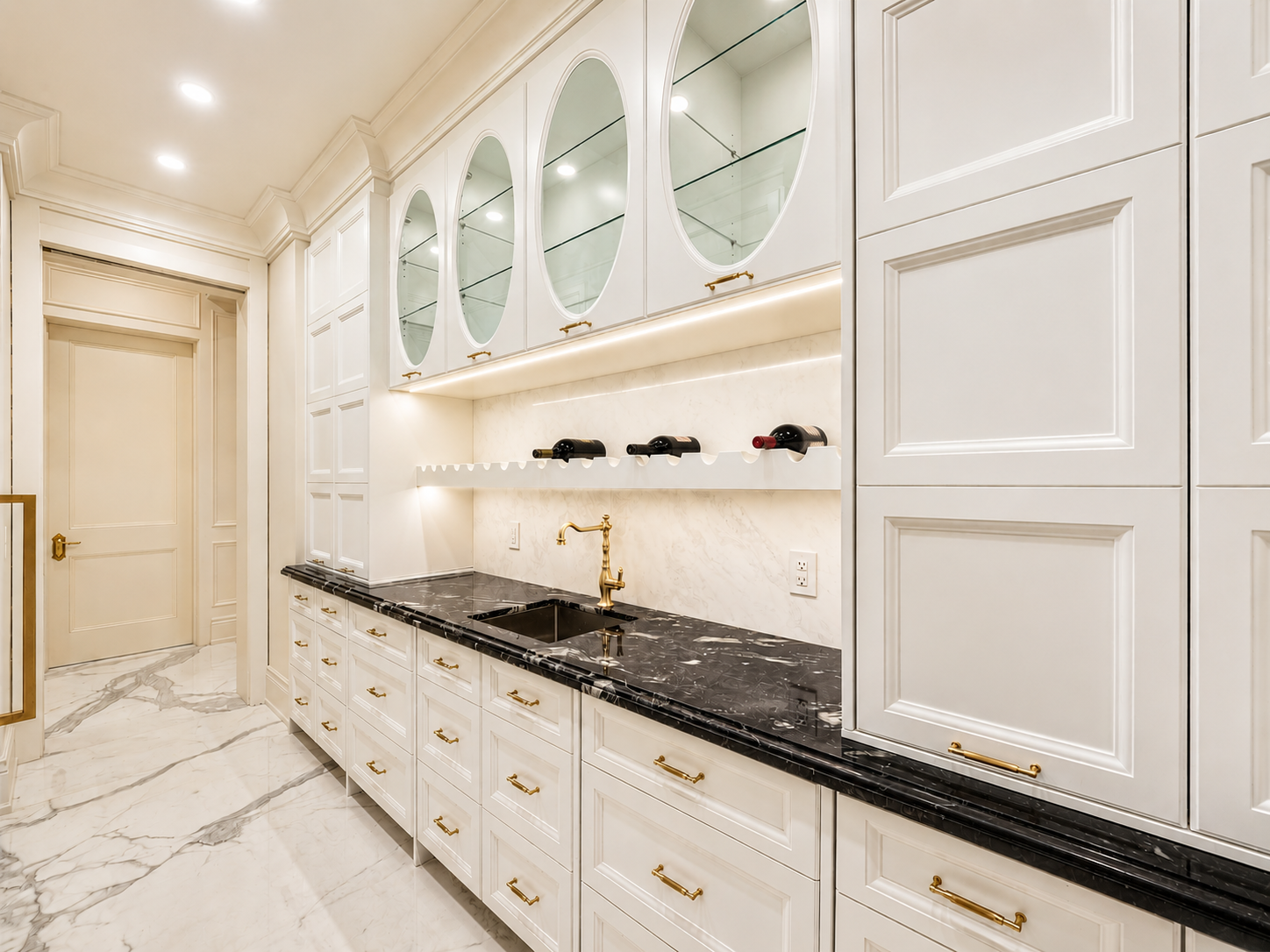 Bright butler’s pantry with white cabinetry, black countertops, display cabinets, and wine storage