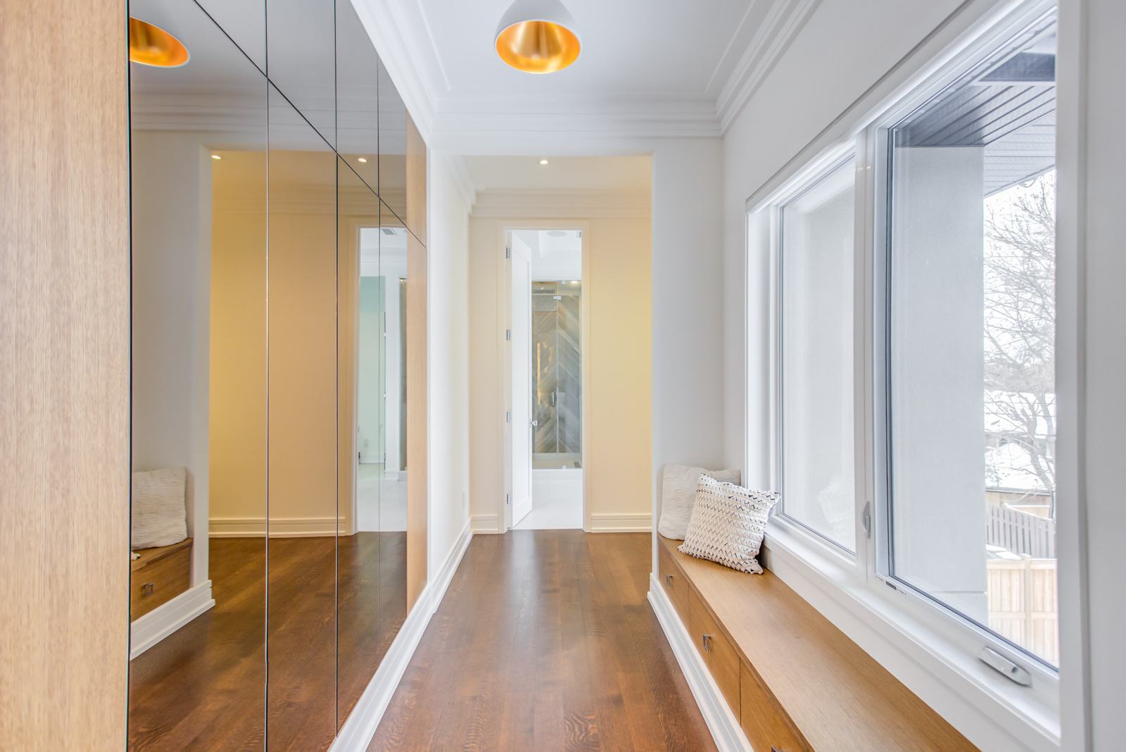 Bright hallway with mirrored wall panels, wood flooring, and built-in window bench