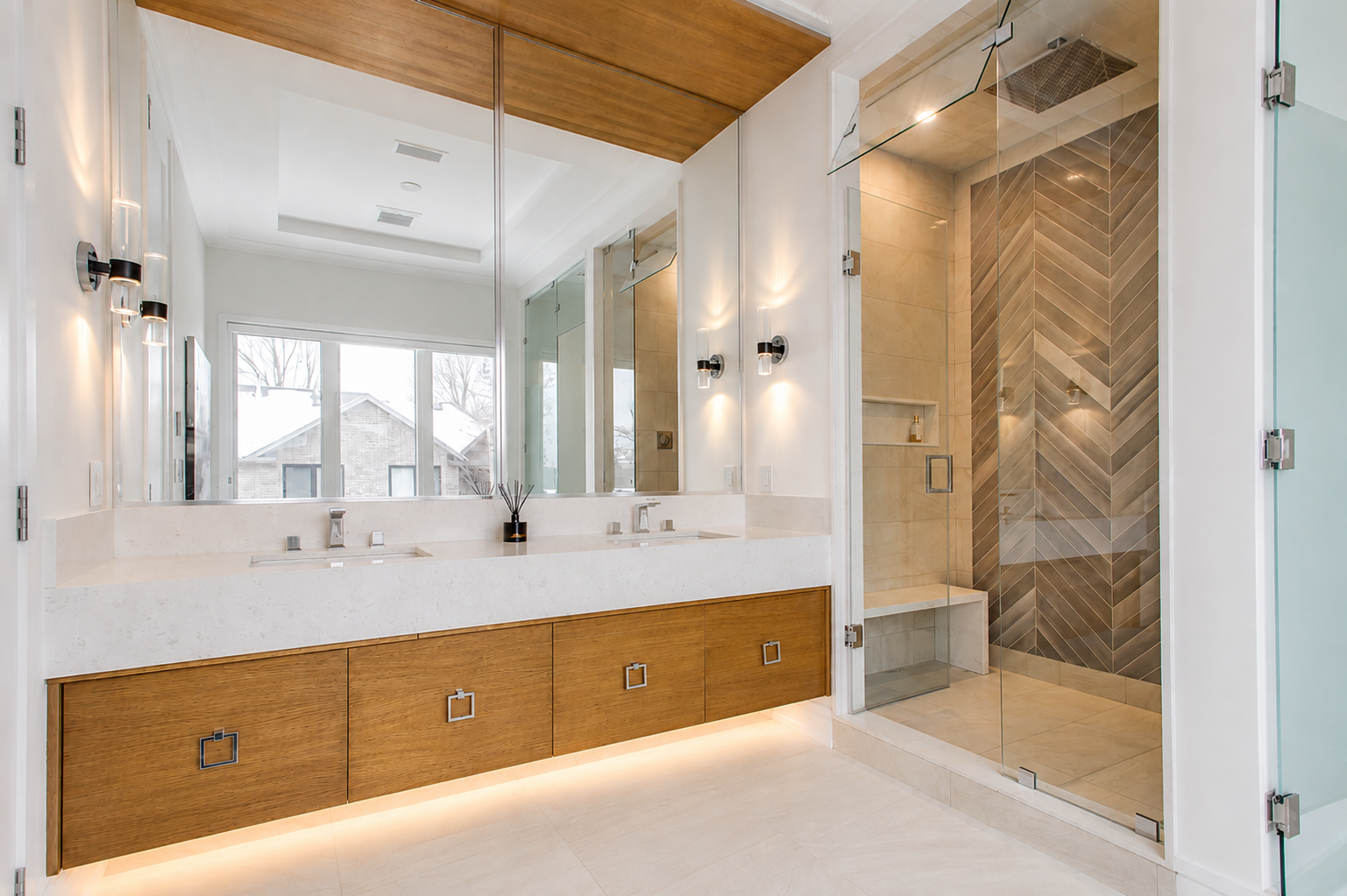 Modern bathroom with long wood vanity, glass shower, chevron tile, and integrated lighting