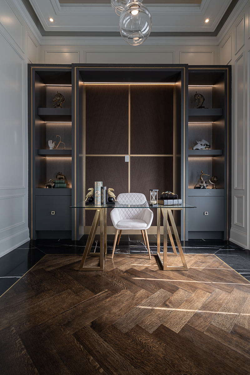 Home office with glass desk, dark wood built-in shelving, and integrated lighting