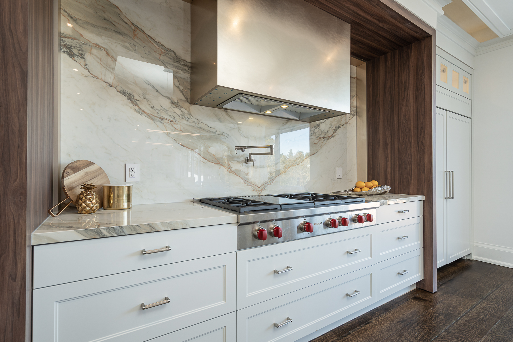Close-up of white kitchen cabinetry, professional range, marble backsplash, and dark wood trim