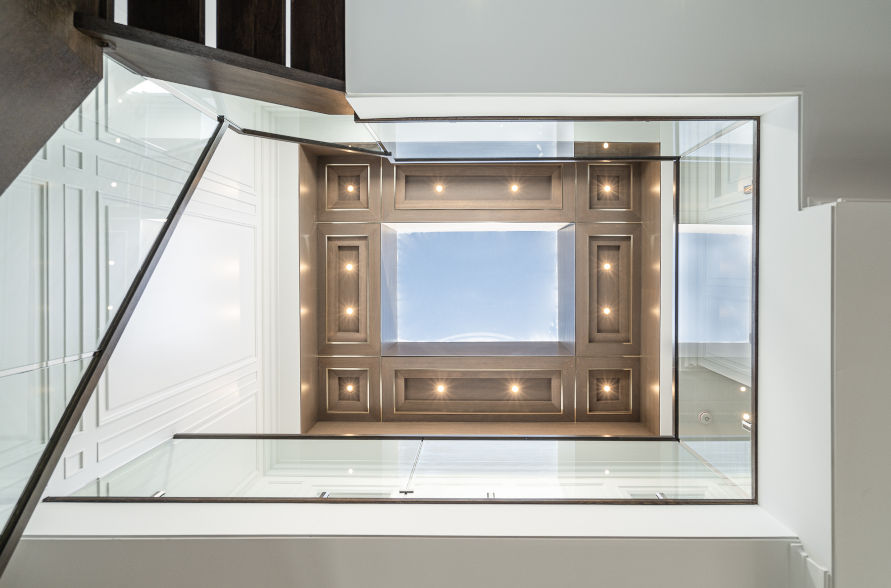 Double-height ceiling opening with glass railing, dark wood detailing, and recessed lighting