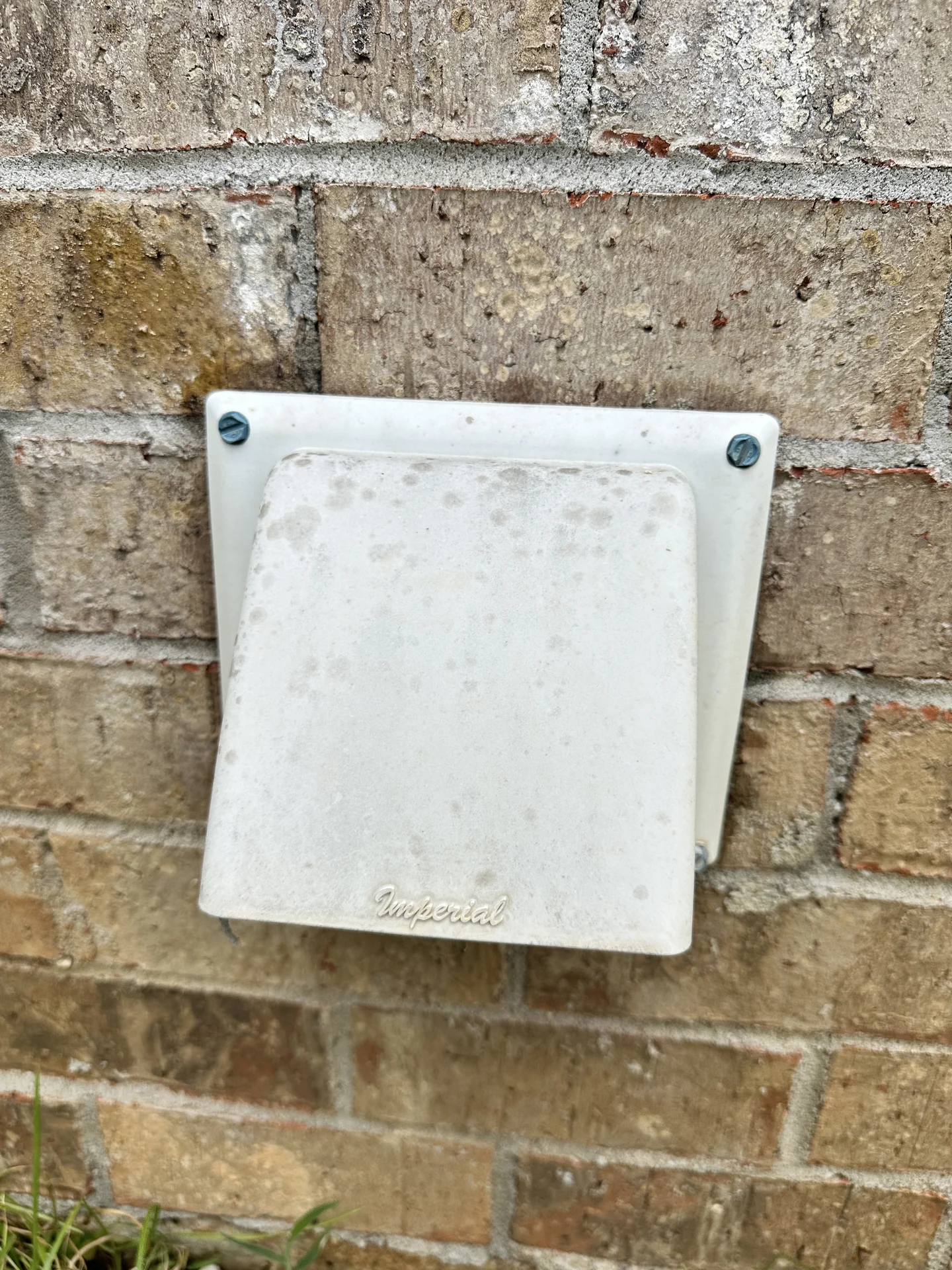 Exterior dryer vent termination on a brick home.