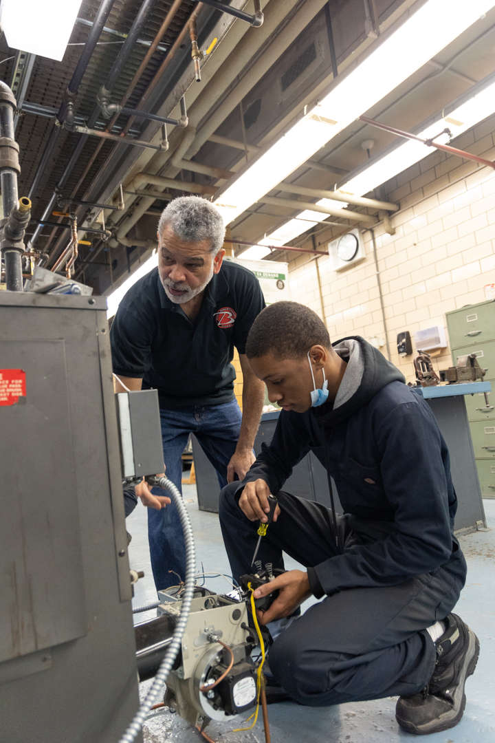 Instructor supervising student working on HVAC equipment in shop class