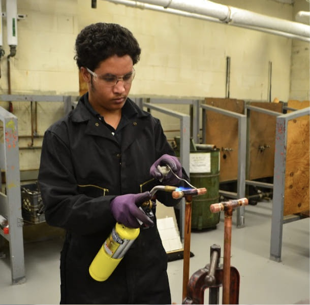 Student soldering copper pipes with a torch in shop class