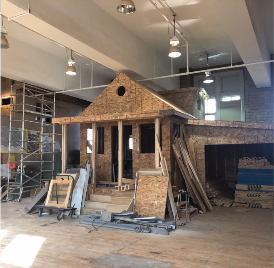 Students building a full-scale wooden house structure indoors