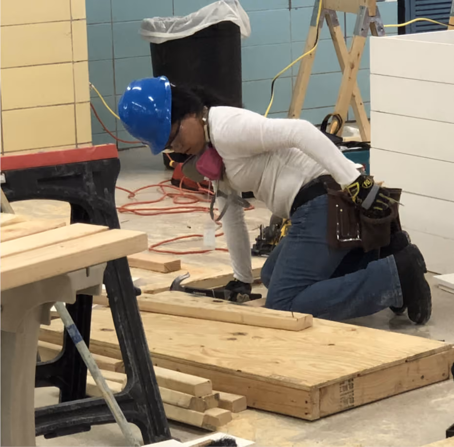 Student wearing hard hat and respirator working with lumber in carpentry class
