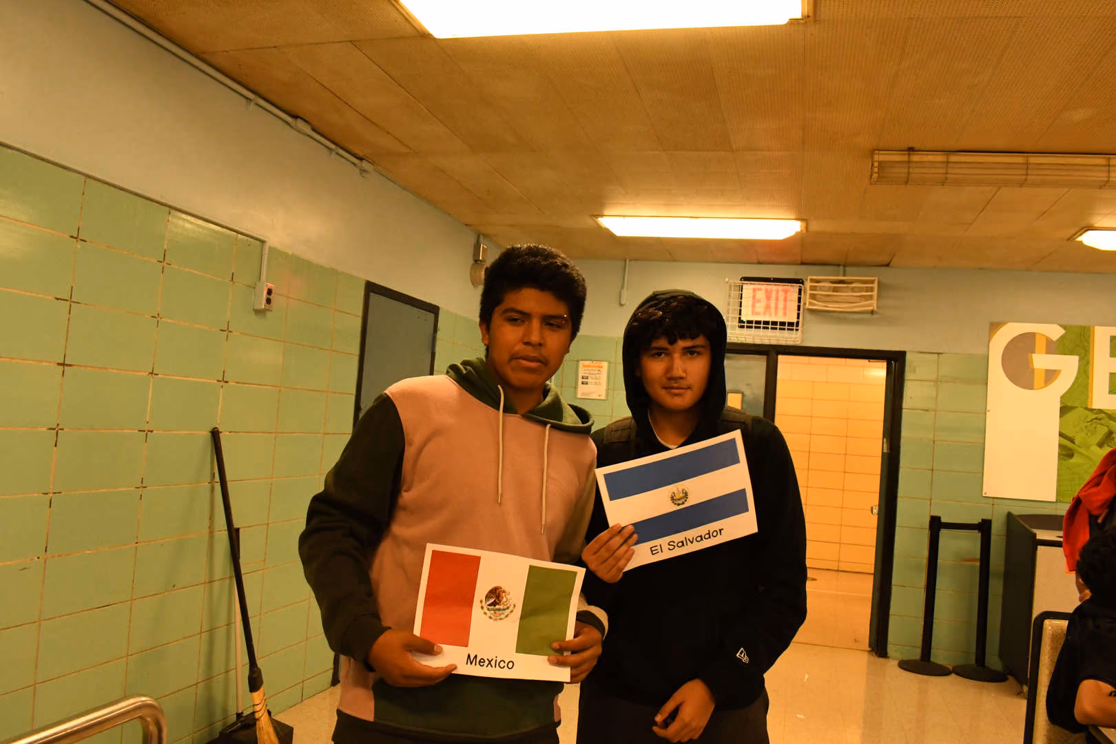Two students holding Mexico and El Salvador flag cards in school hallway