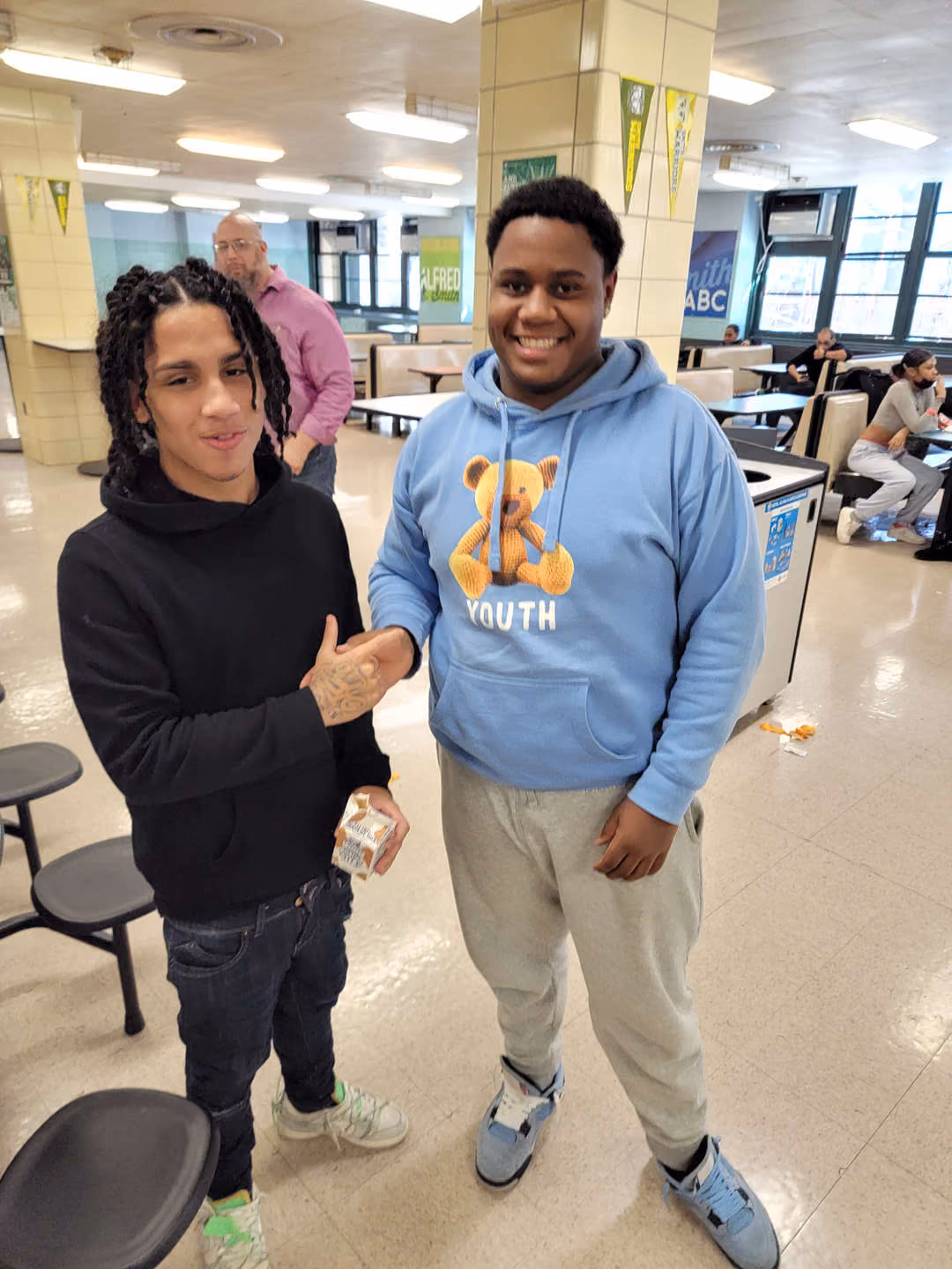 Two students shaking hands and smiling in school cafeteria