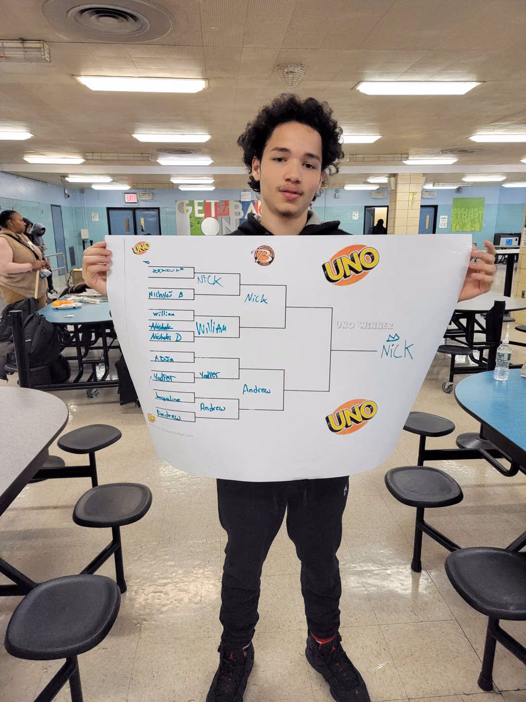 Student holding UNO tournament bracket showing Nick as the winner