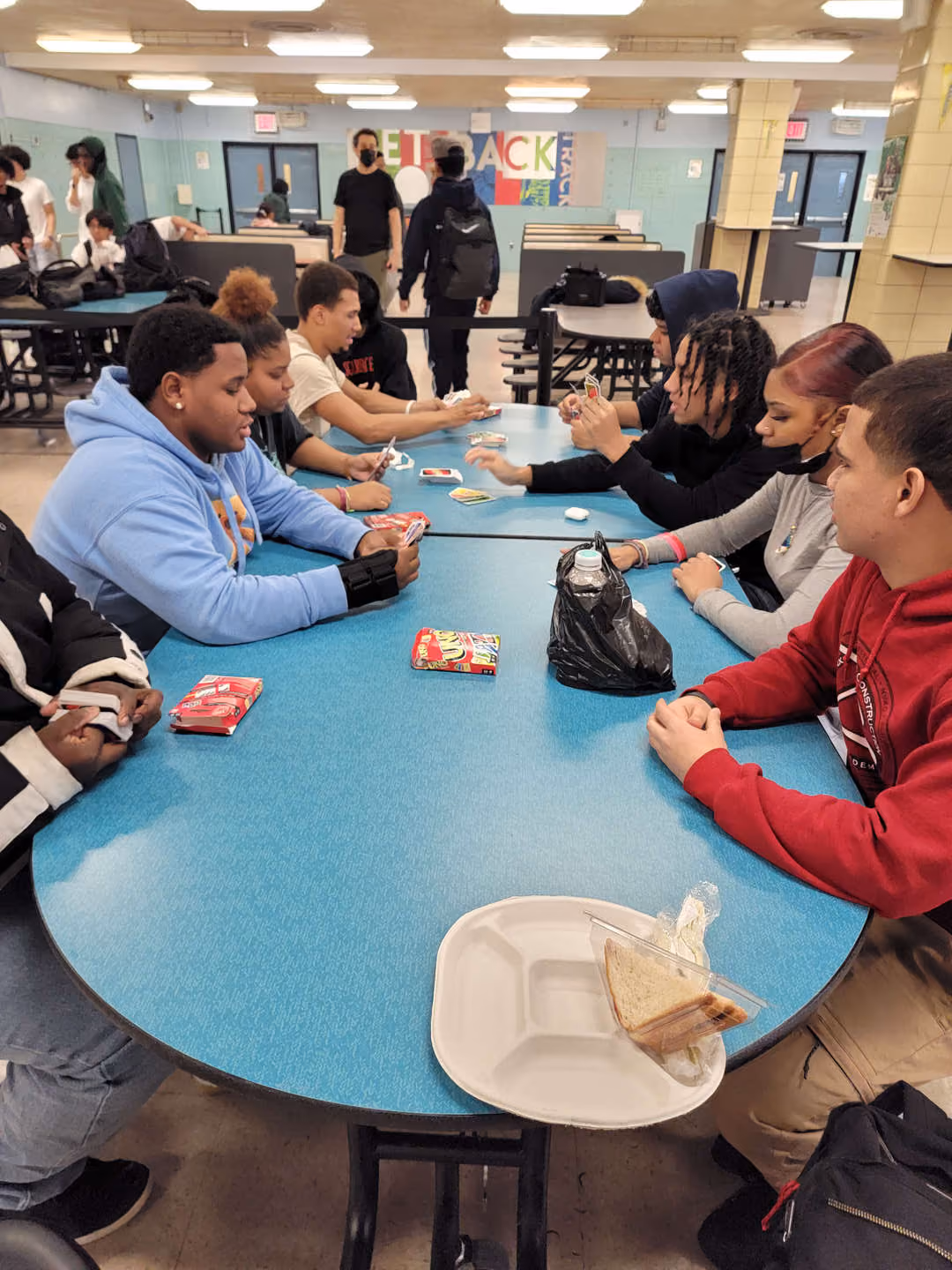Students socializing and playing cards in school cafeteria at lunch