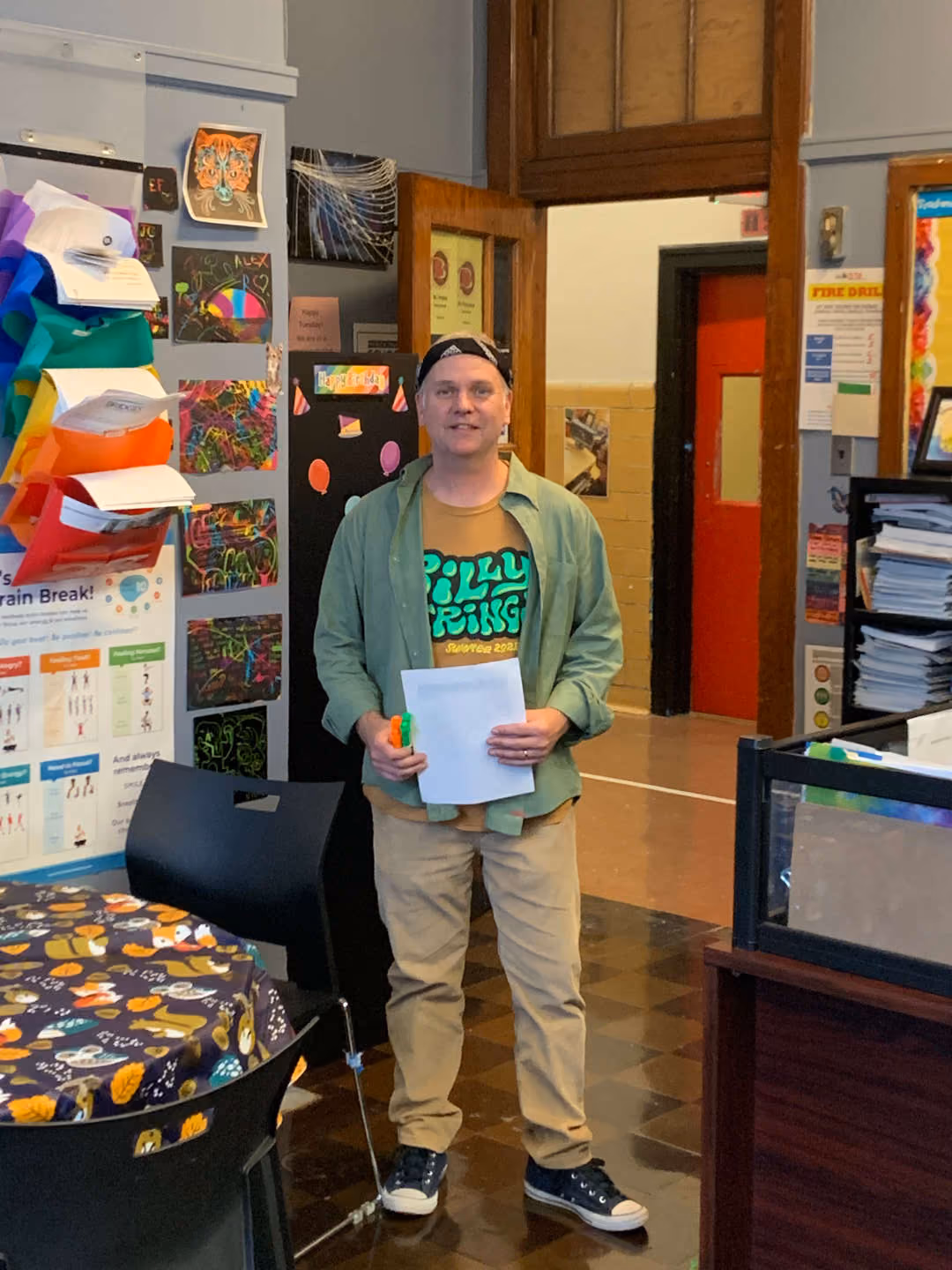 Teacher holding papers stands in a decorated classroom hallway